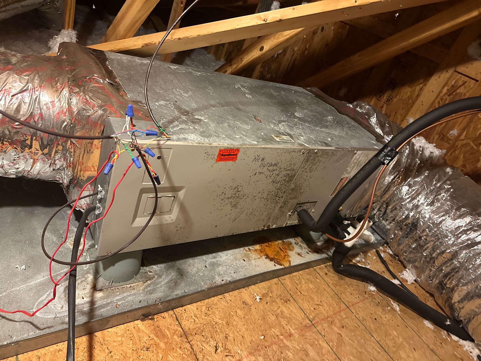 A dirty air conditioner is sitting in the attic of a house.