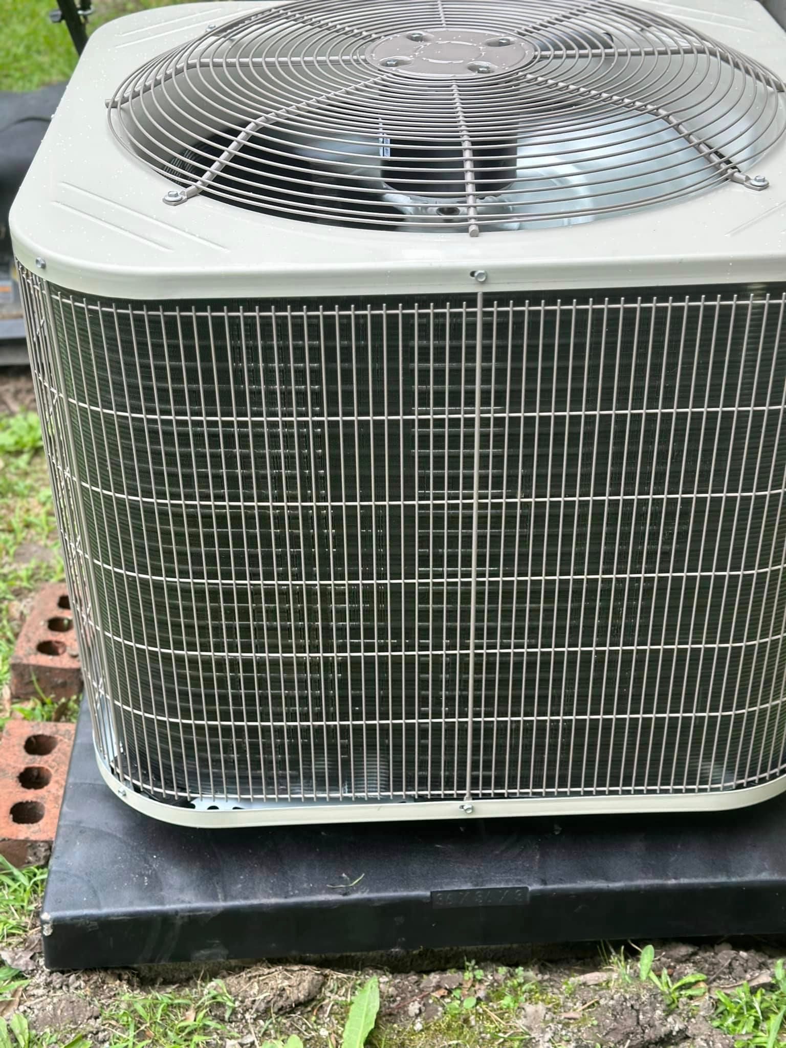 A large air conditioner is sitting on top of a black pallet in the grass