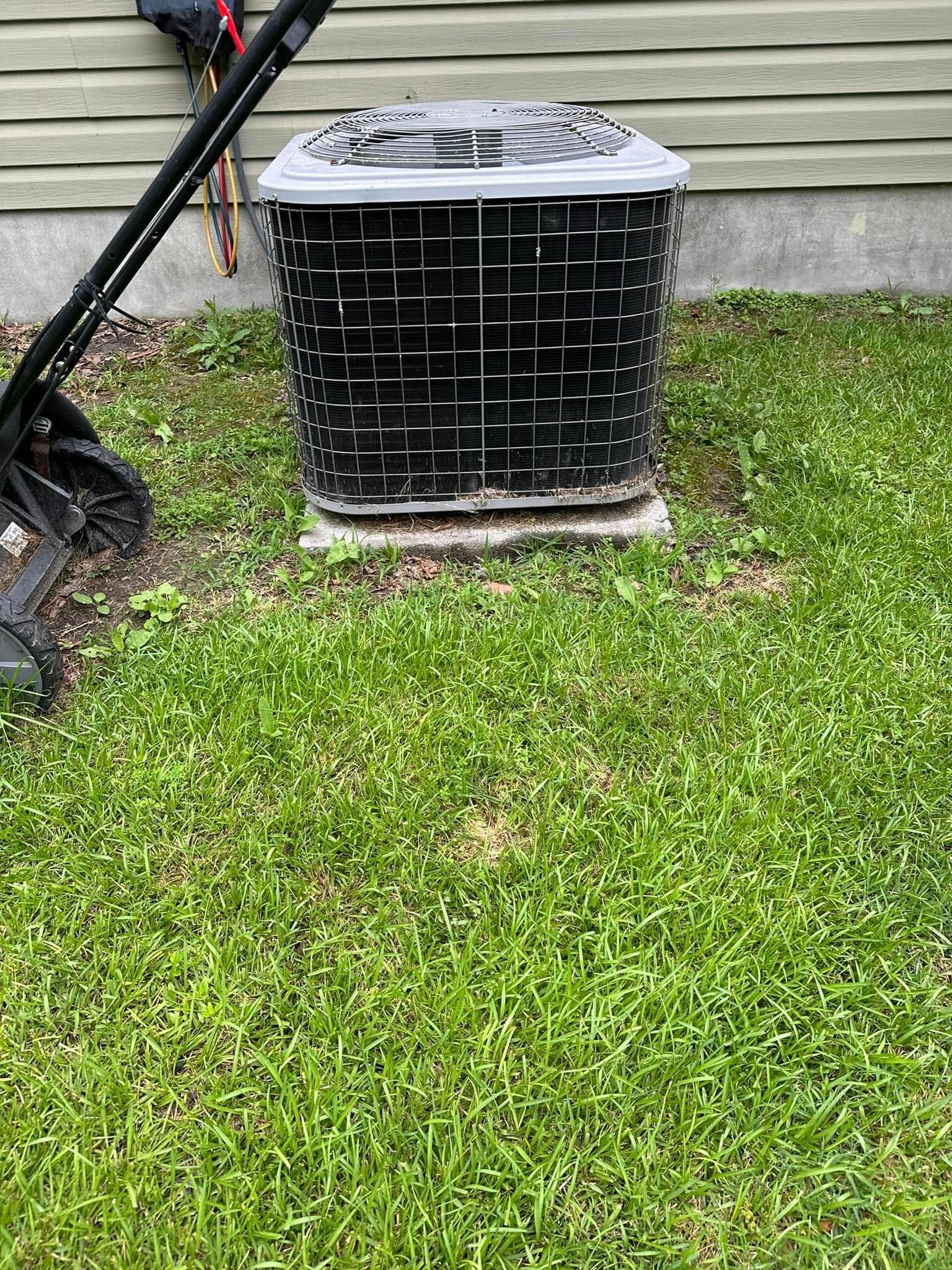 An air conditioner is sitting in the grass in front of a house