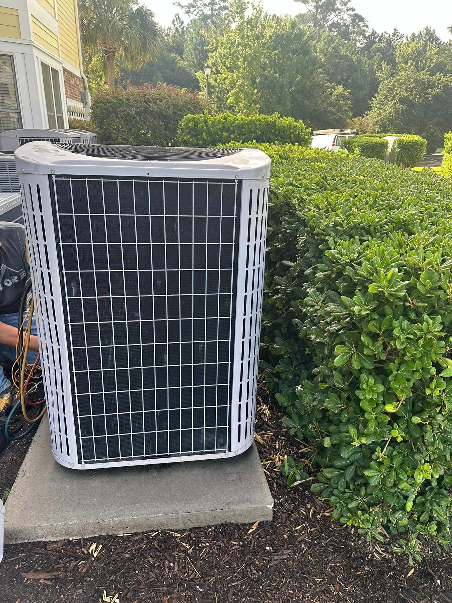 A person is working on an air conditioner in a yard