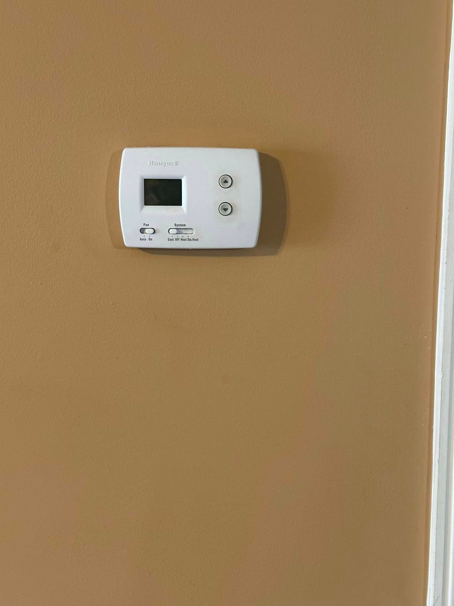 A white thermostat is hanging on a brown wall