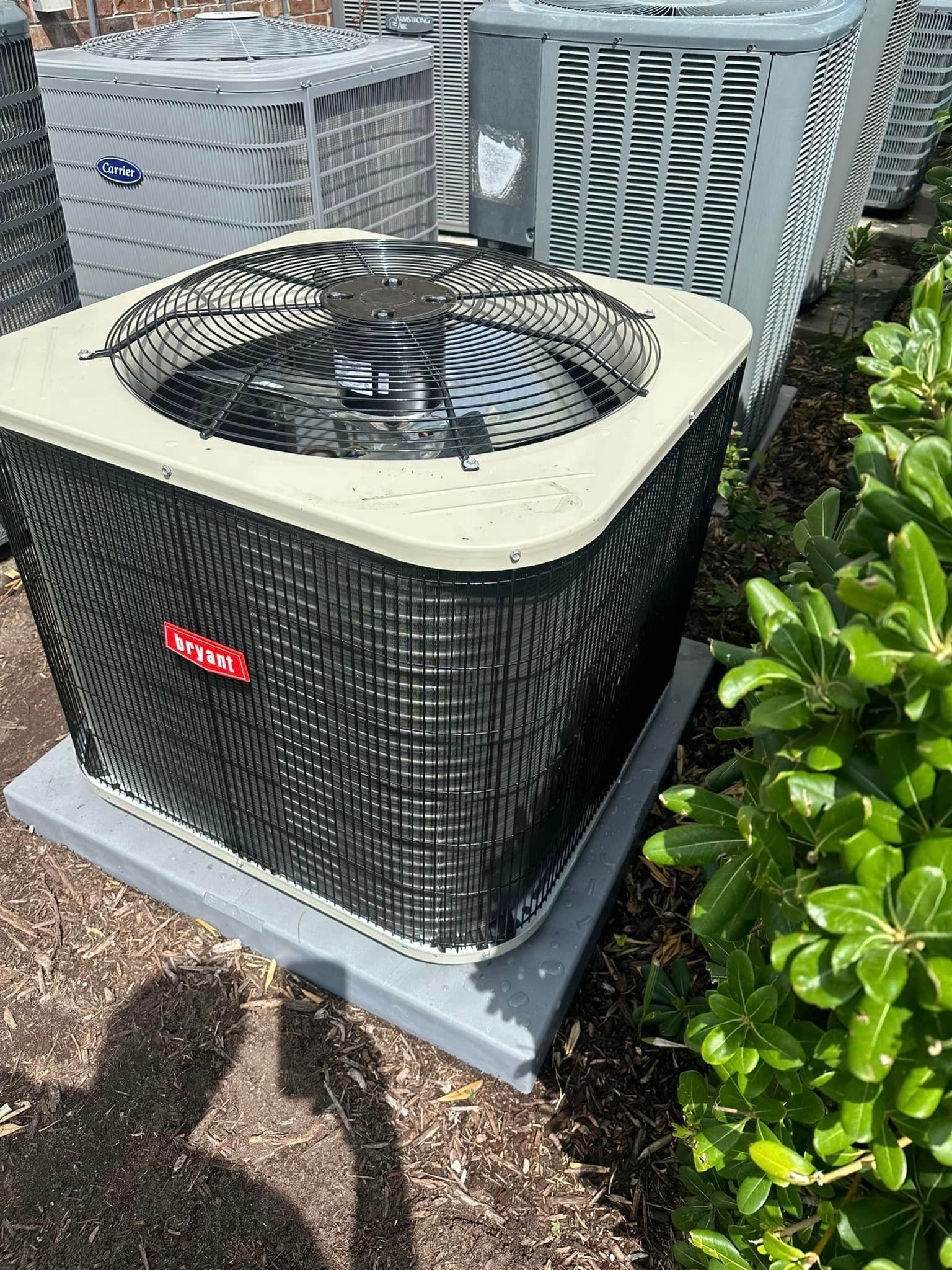 A large air conditioner is sitting on top of a concrete platform next to a bush.
