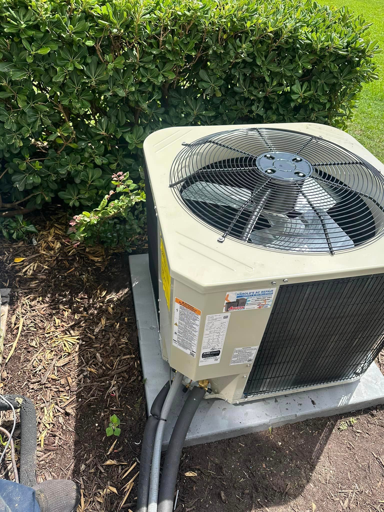 A large air conditioner is sitting in the dirt next to a bush.