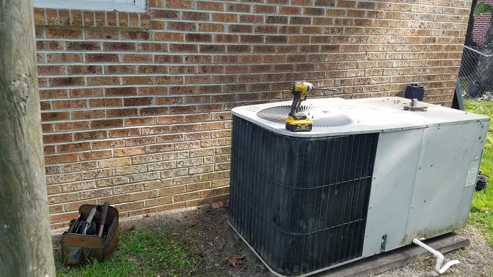 An air conditioner is sitting on the ground next to a brick wall