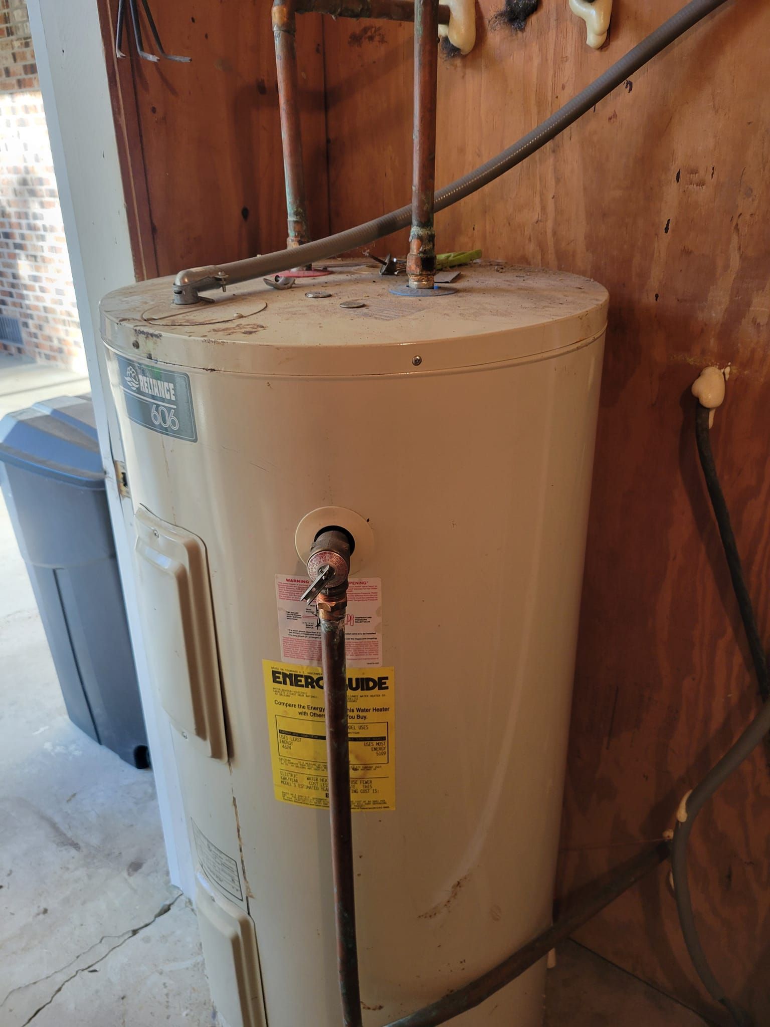 A white water heater is sitting next to a wooden wall
