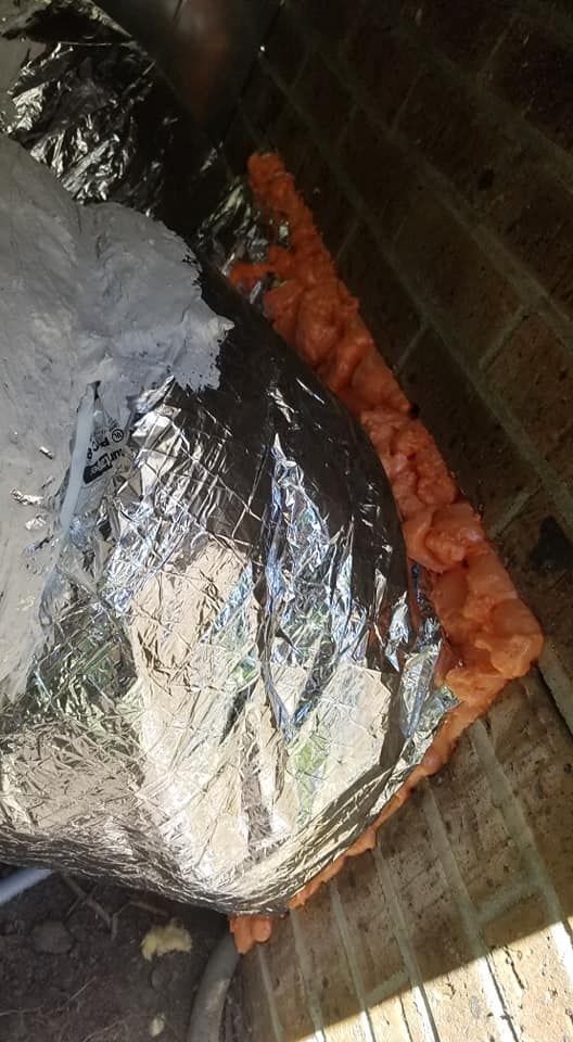 A close up of a duct with aluminum foil and foam on a brick wall