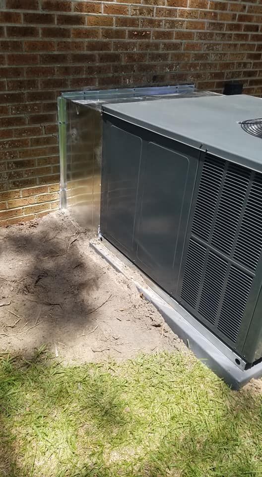 A large air conditioner is sitting in the dirt next to a brick wall