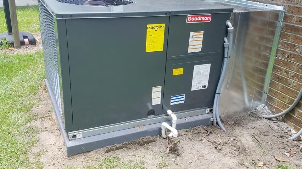 An air conditioner is sitting in the dirt next to a brick wall