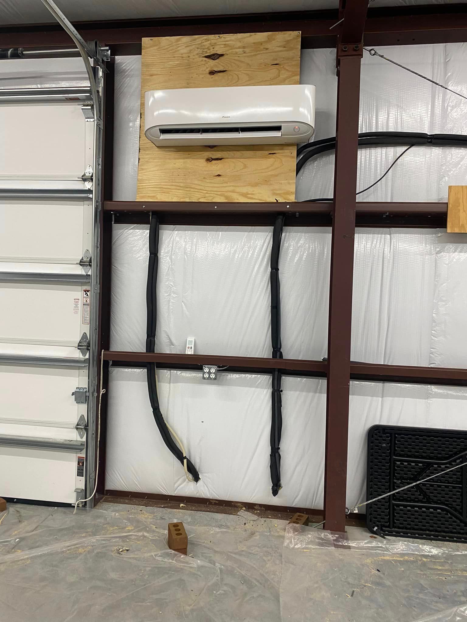 A white air conditioner is mounted on a wall next to a garage door