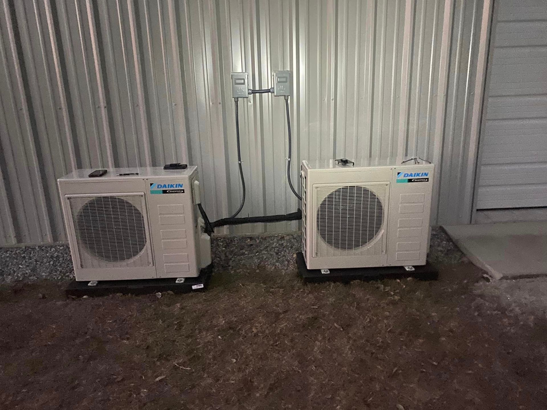 Two air conditioners are sitting next to each other in front of a garage door