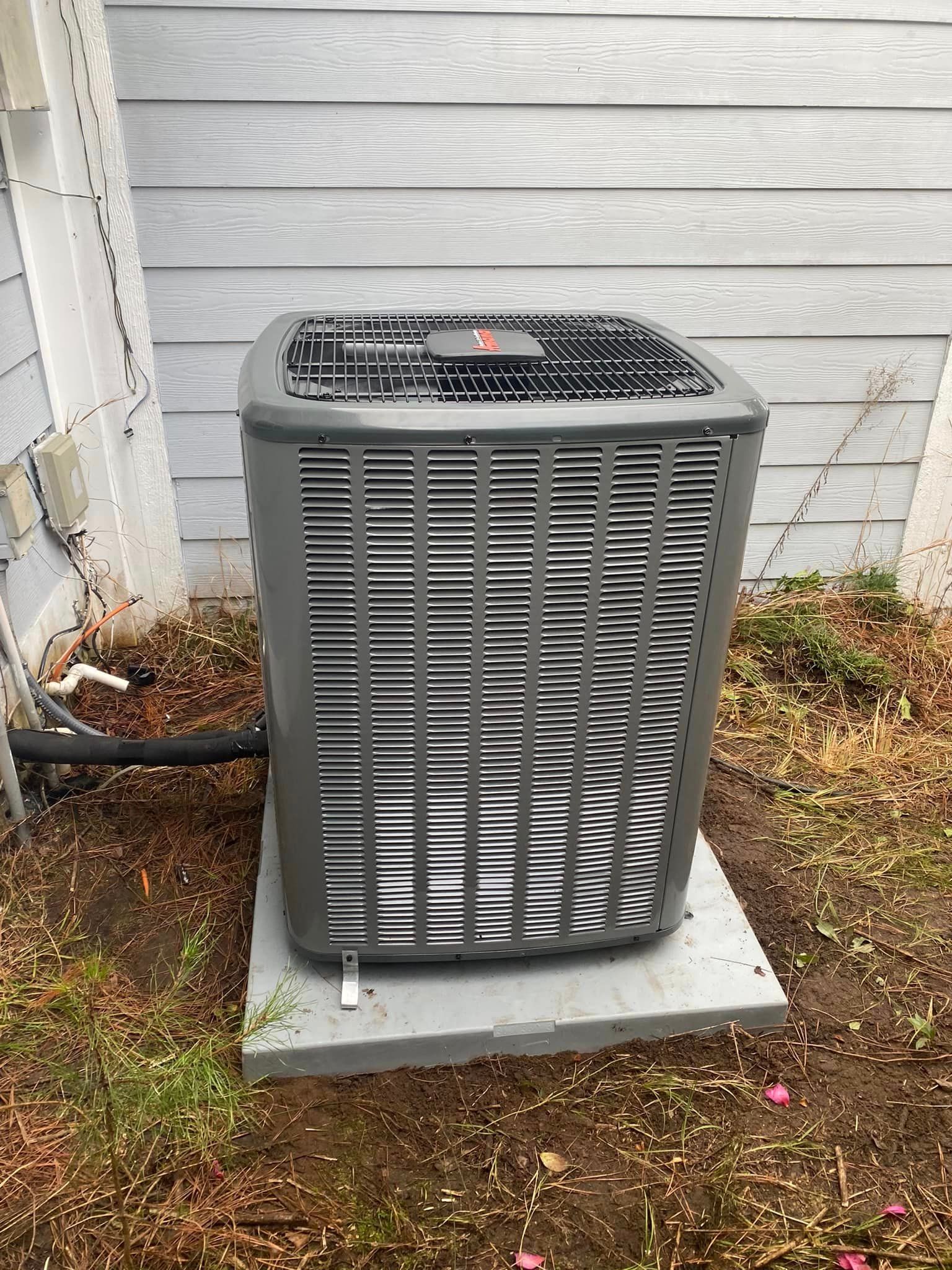 A large air conditioner is sitting on top of a concrete platform in the backyard of a house