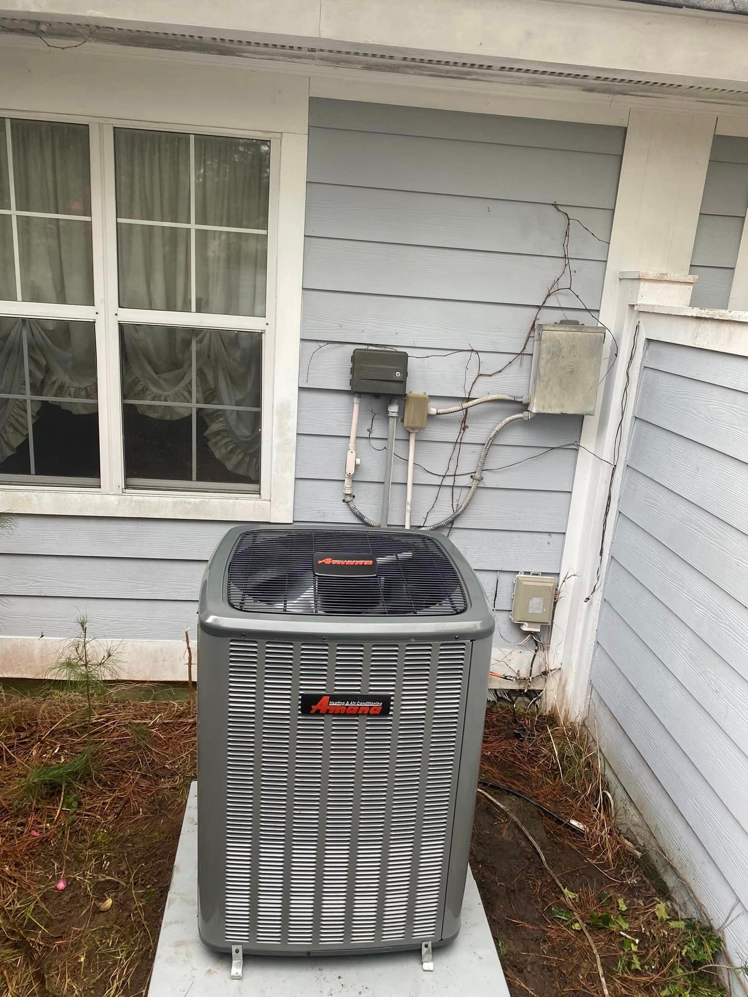 An air conditioner is sitting outside of a house next to a window