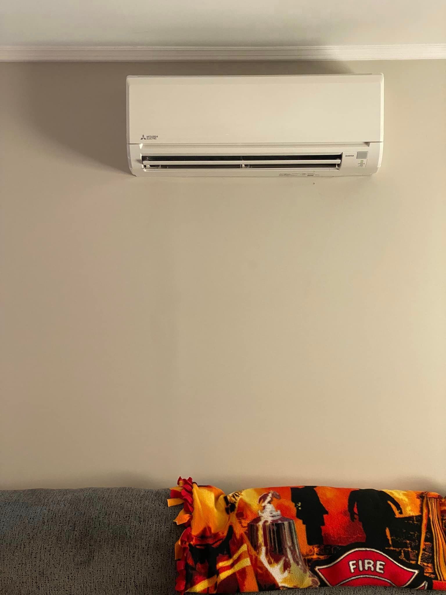 A wall-mounted air conditioner is hanging from the ceiling above a bed