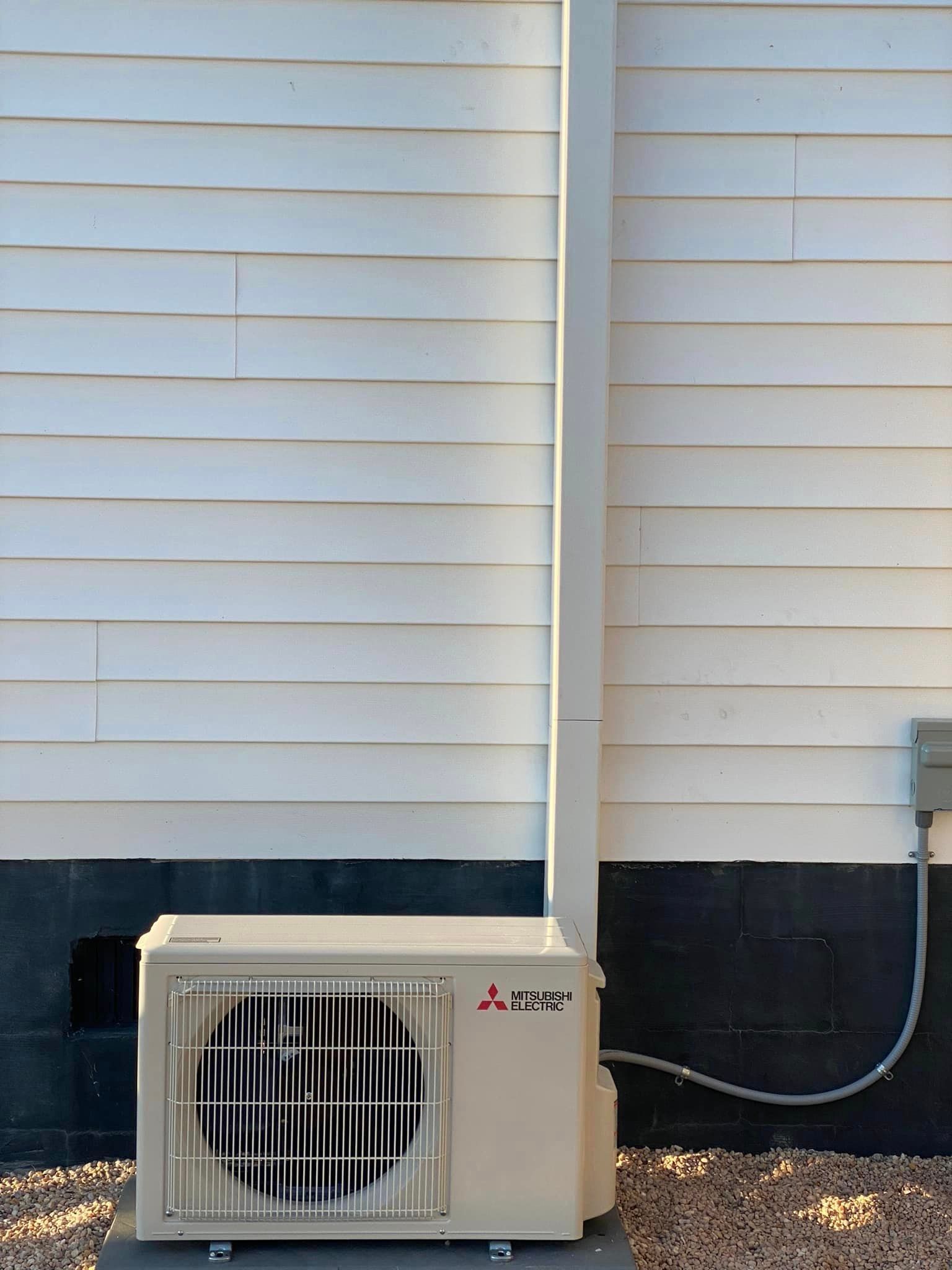 A mitsubishi air conditioner is sitting outside of a white house