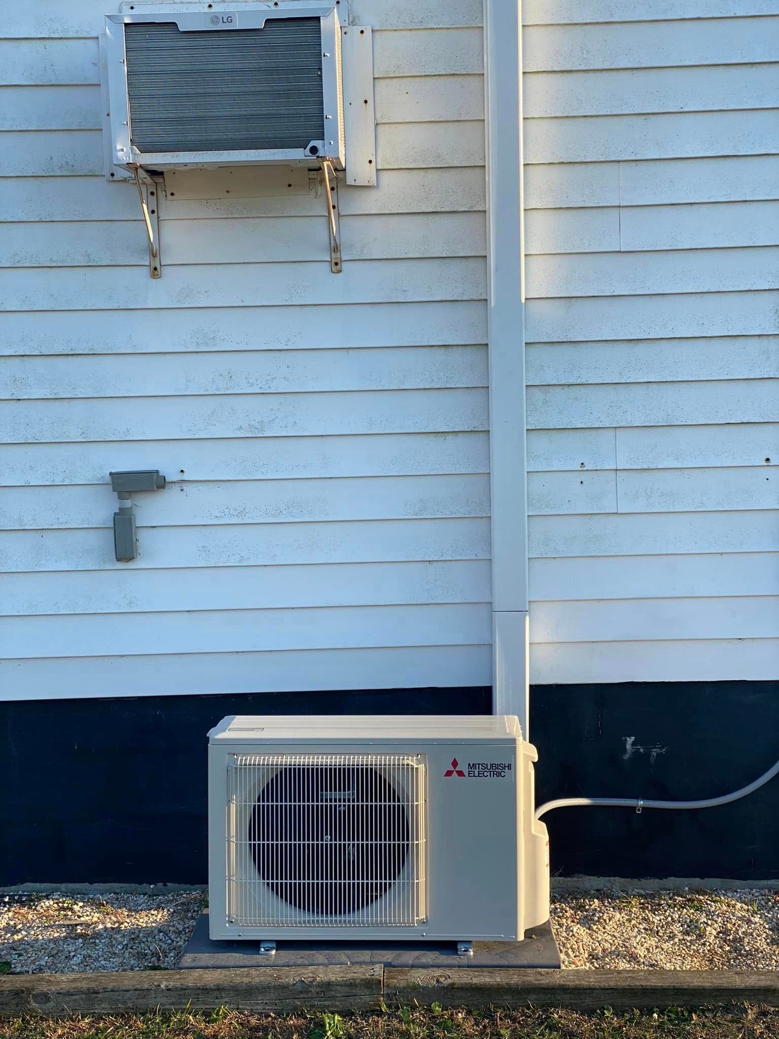 A white air conditioner is mounted on the side of a white house