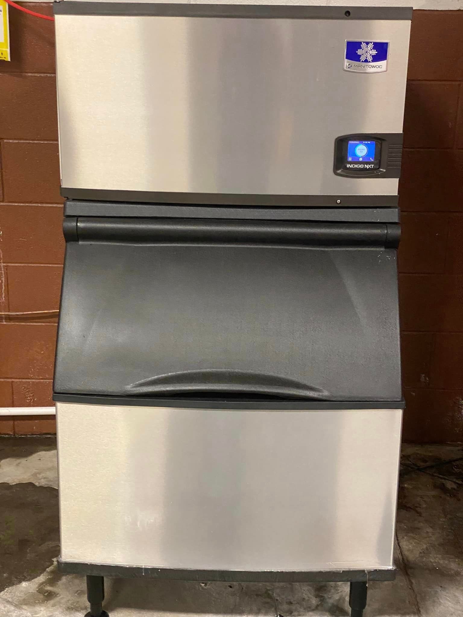 A stainless steel ice machine is sitting in front of a brick wall