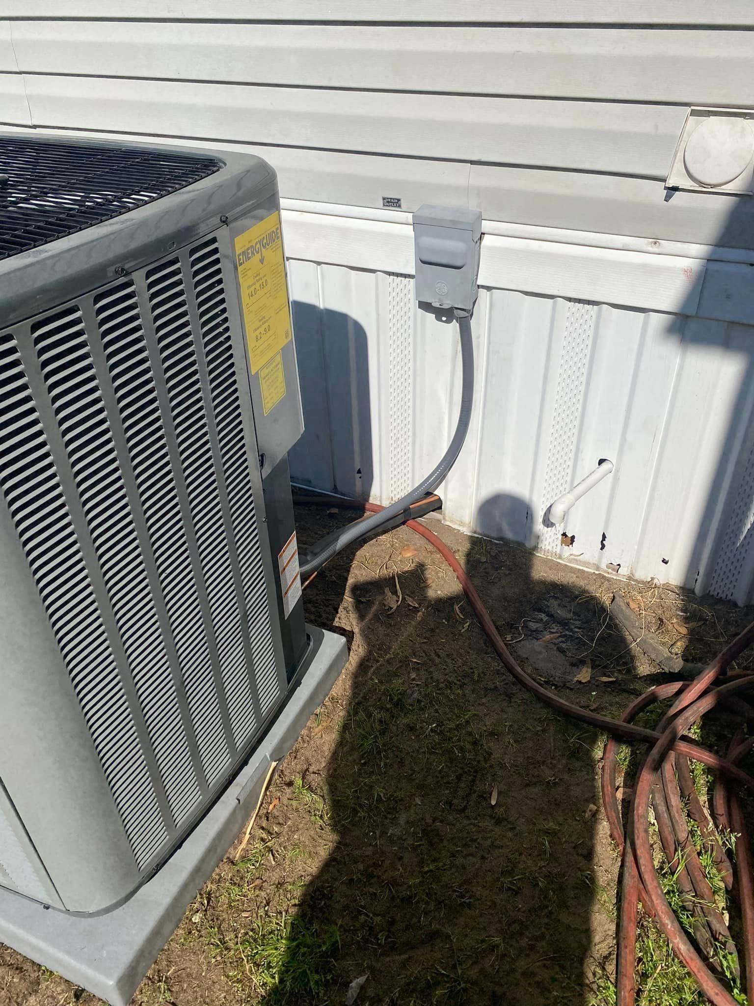 An air conditioner is sitting on the side of a house next to a hose