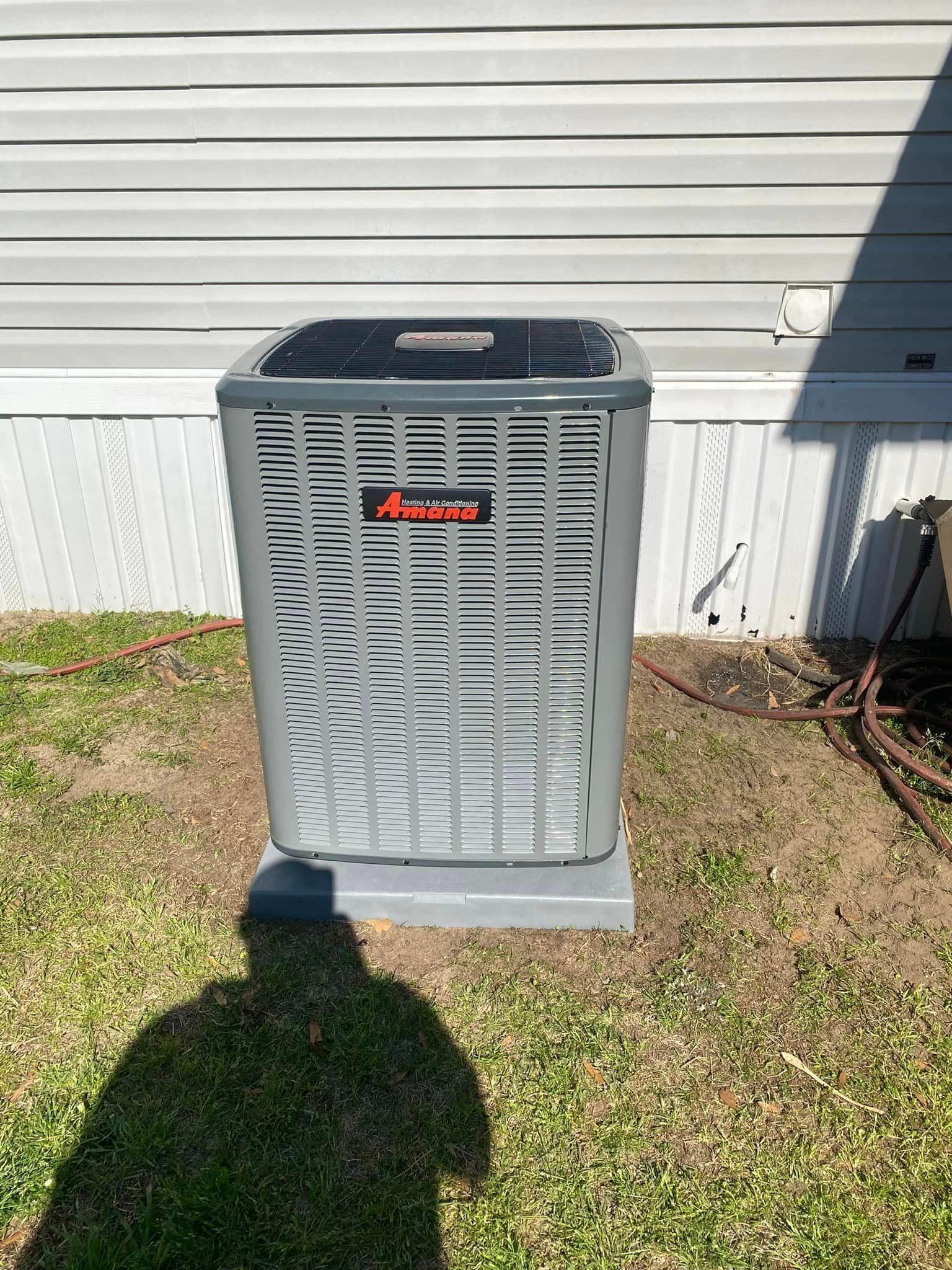 A gray air conditioner is sitting in the grass in front of a house