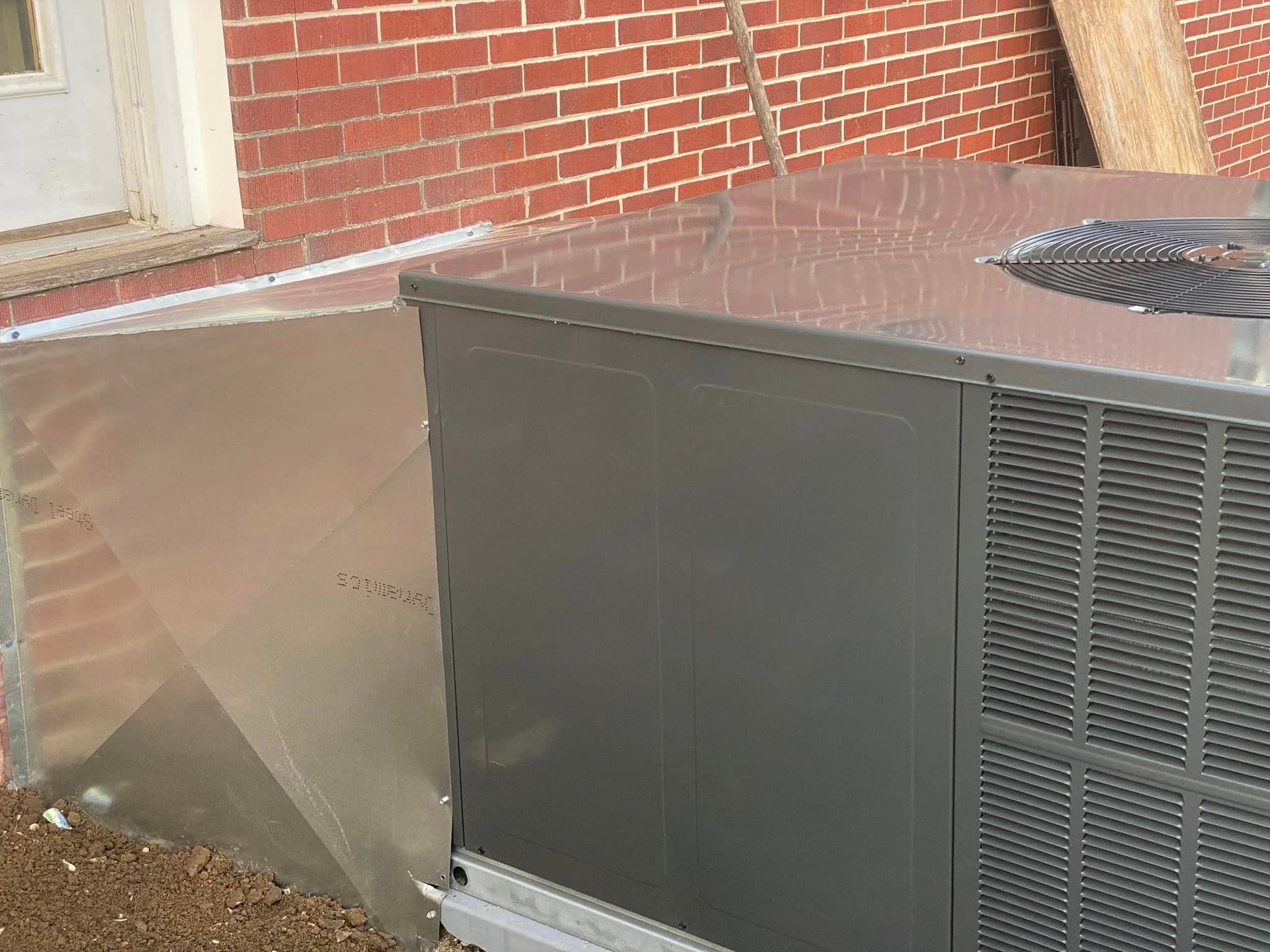 A gray air conditioner is sitting in front of a brick building