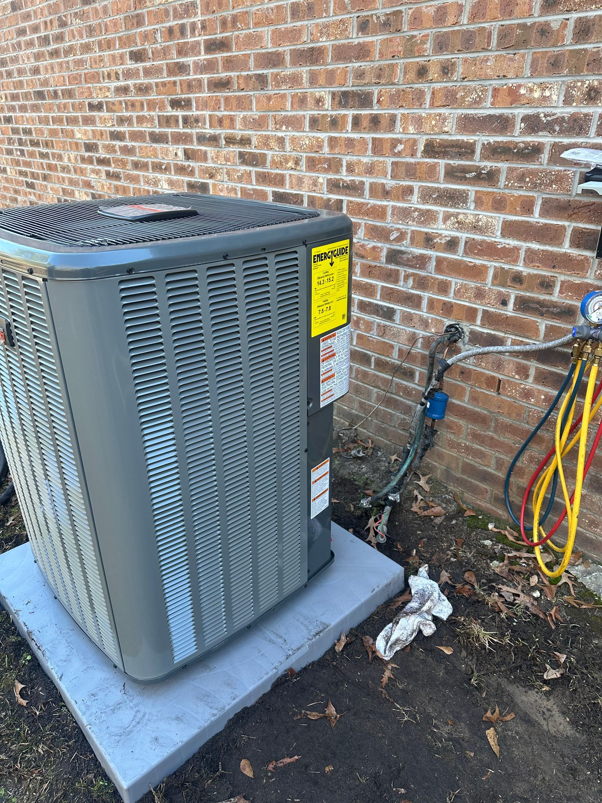 A large air conditioner is sitting on top of a concrete platform next to a brick wall.