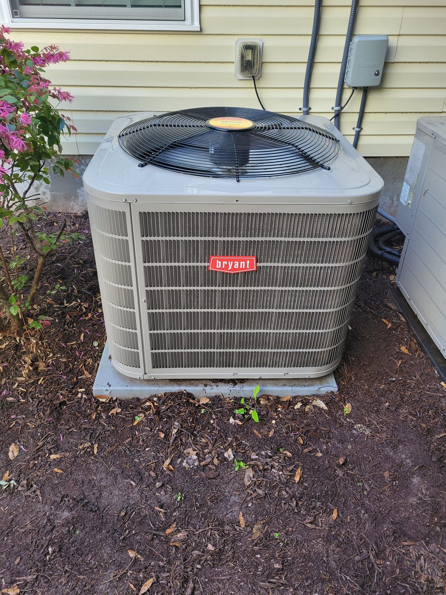 A large air conditioner is sitting in the dirt in front of a house
