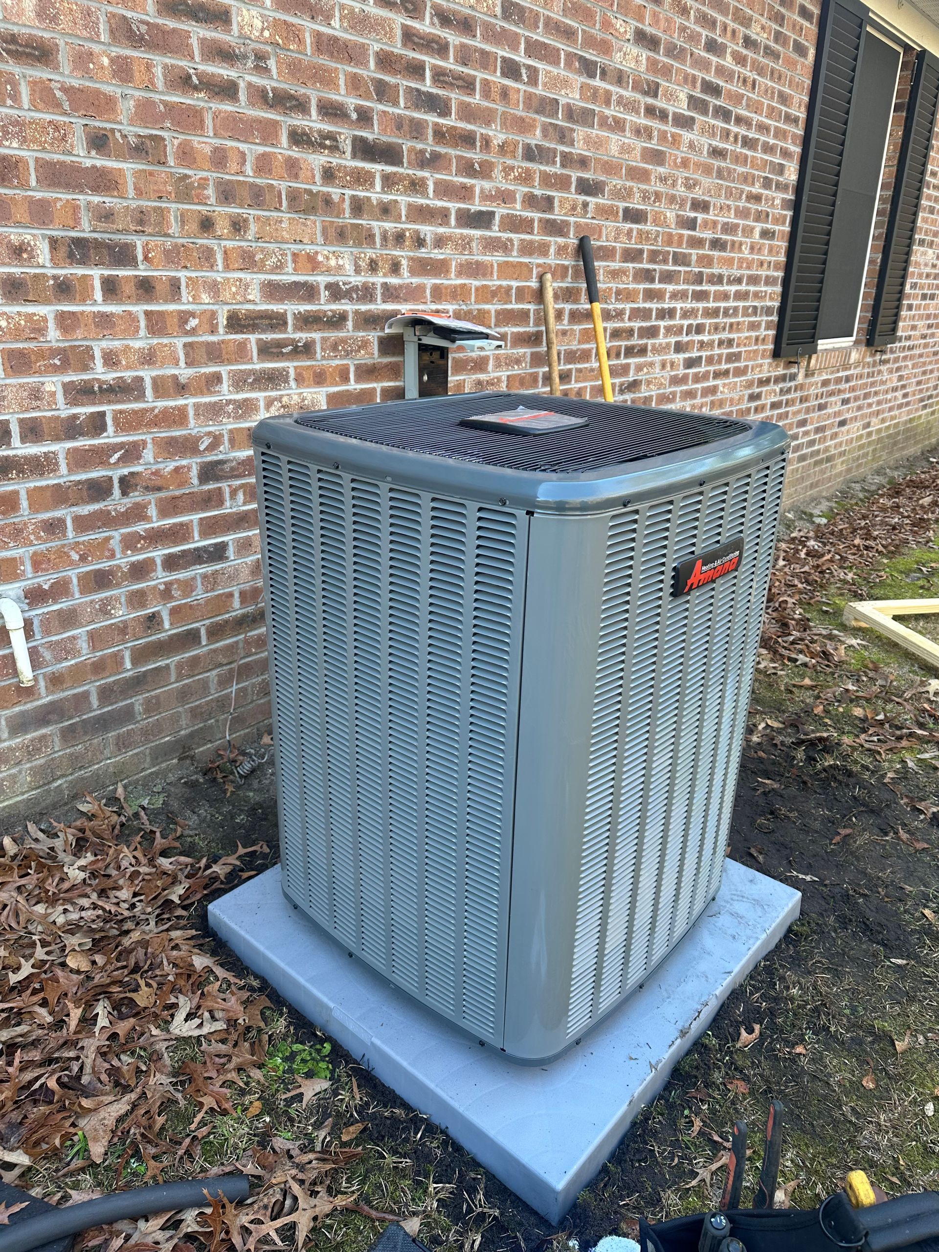 A large air conditioner is sitting on top of a concrete platform in front of a brick building.