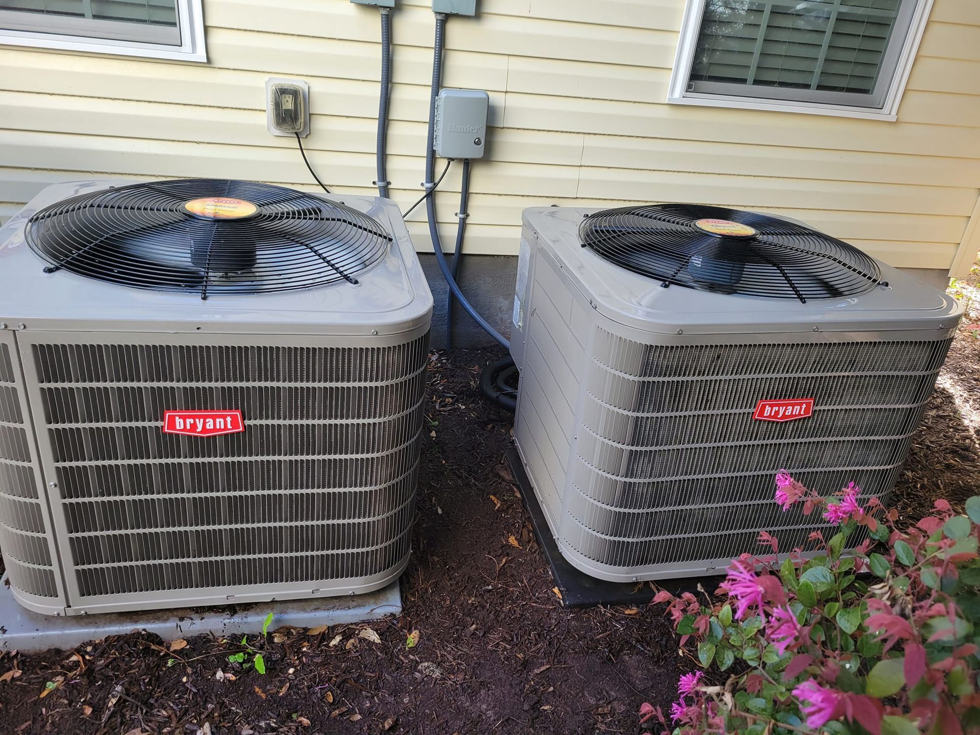 Two air conditioners are sitting next to each other on the side of a house