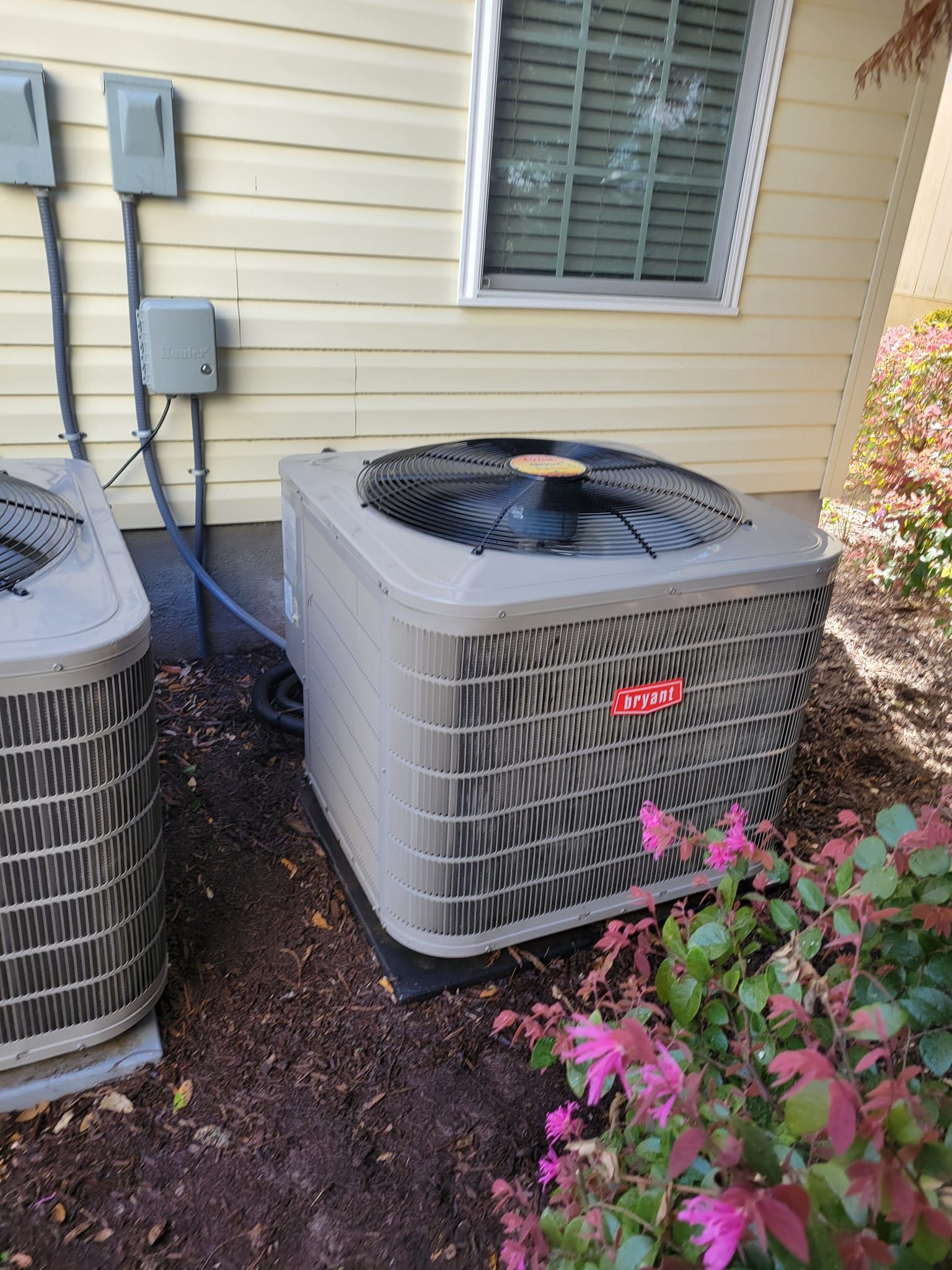 Two air conditioners are sitting next to each other on the side of a house