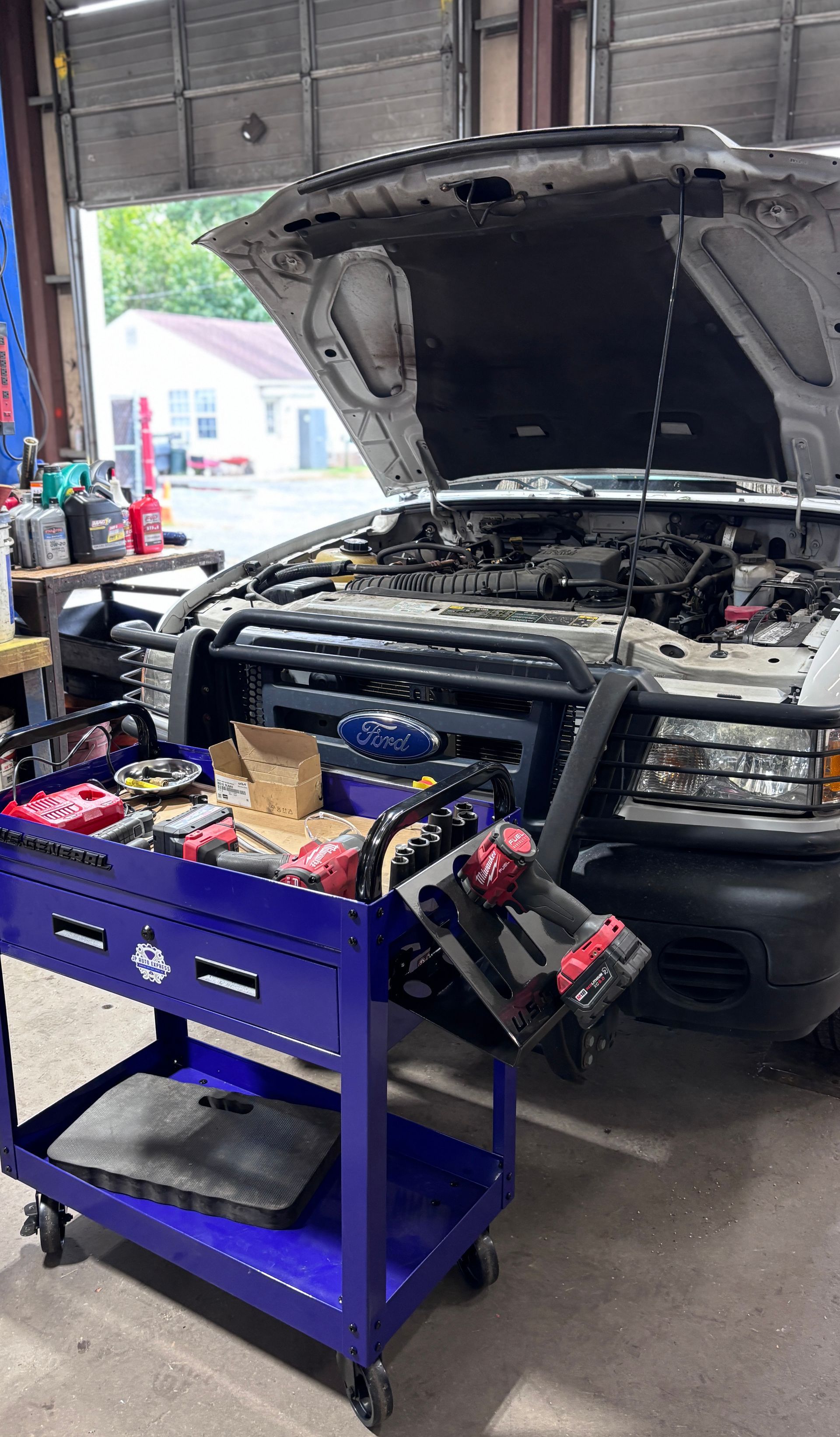 Black SUV in a garage with hood open, surrounded by tools and equipment on a purple cart.