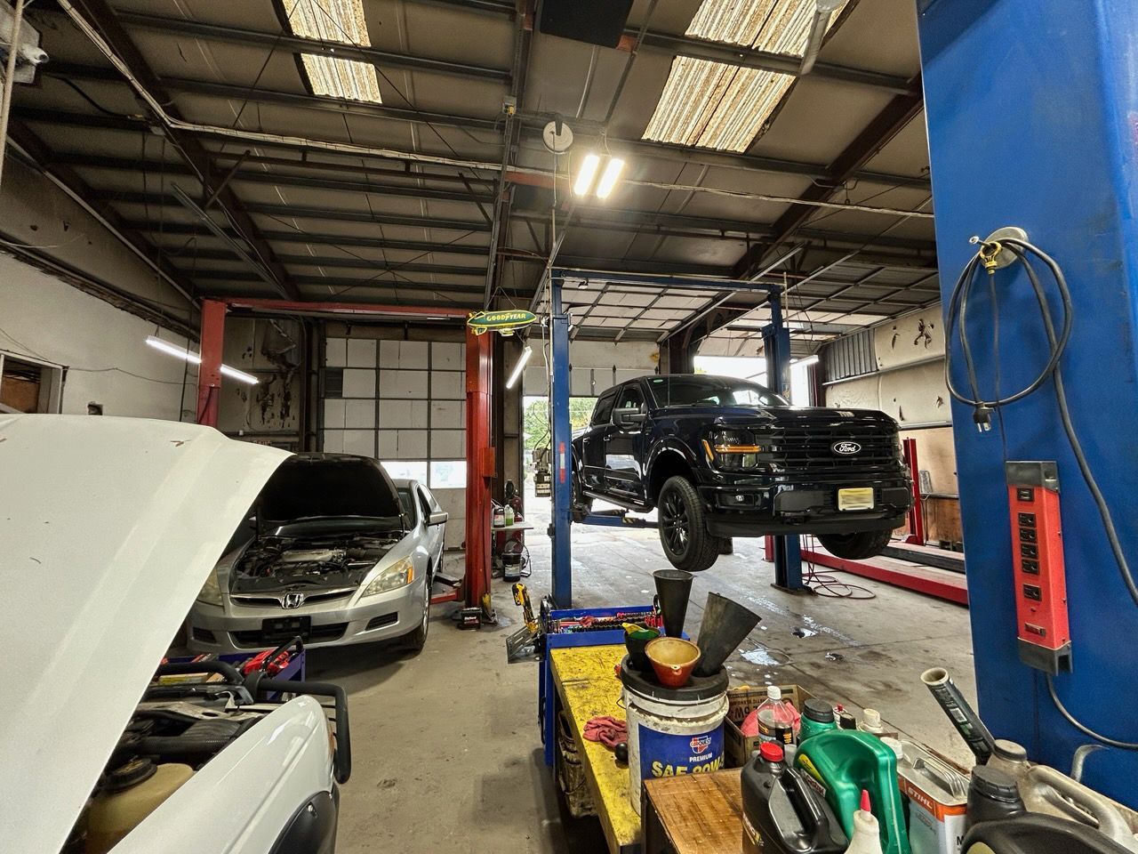 Auto repair shop with a silver car and a black SUV on lifts, tools and supplies in the foreground.