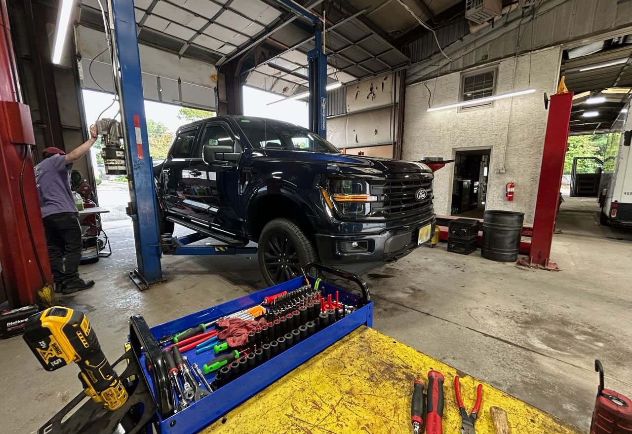 Black pickup truck in an auto repair shop, lifted on a jack inside a garage with tools nearby
