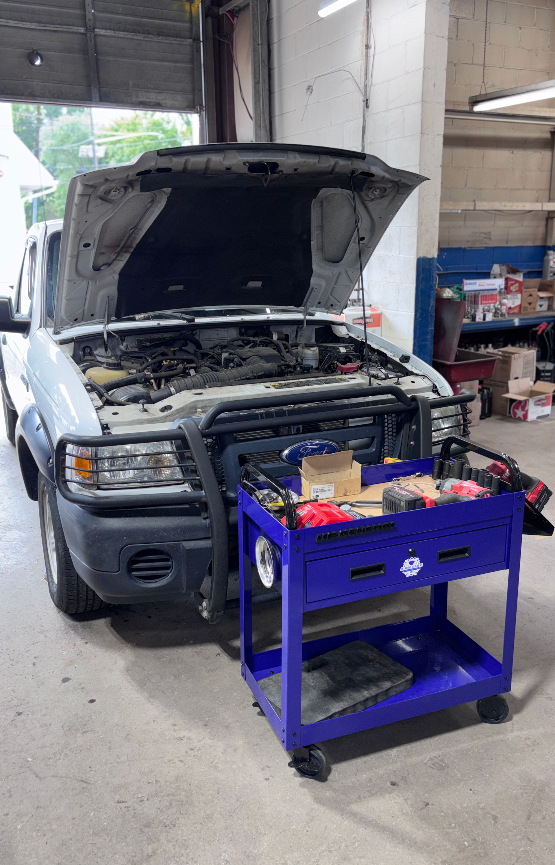 Car with hood open in a garage, with a blue rolling tool cart in front.
