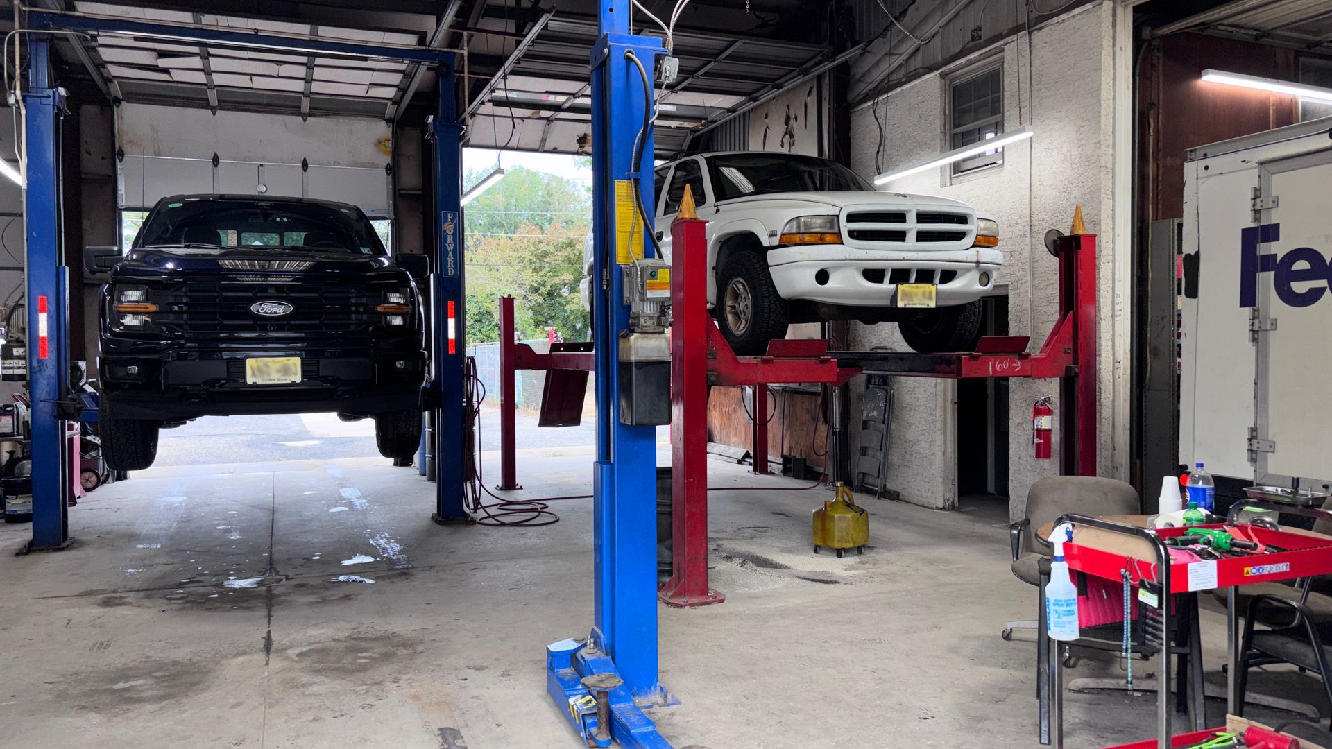 Auto repair shop with two vehicles lifted on car hoists, one black and one white, inside a garage.
