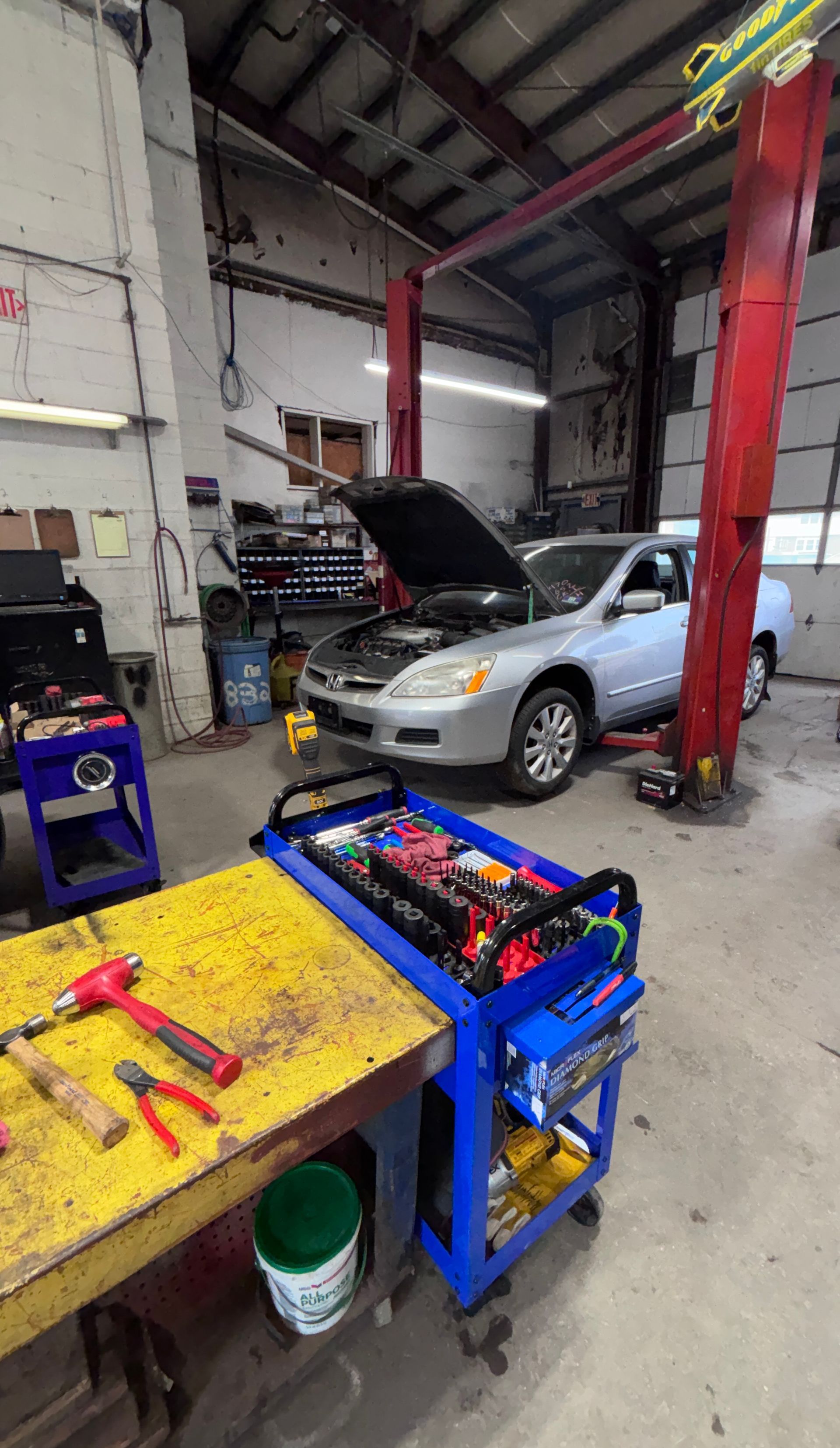 Auto repair shop with silver SUV on lift, hood open, and tools on a workbench in the foreground