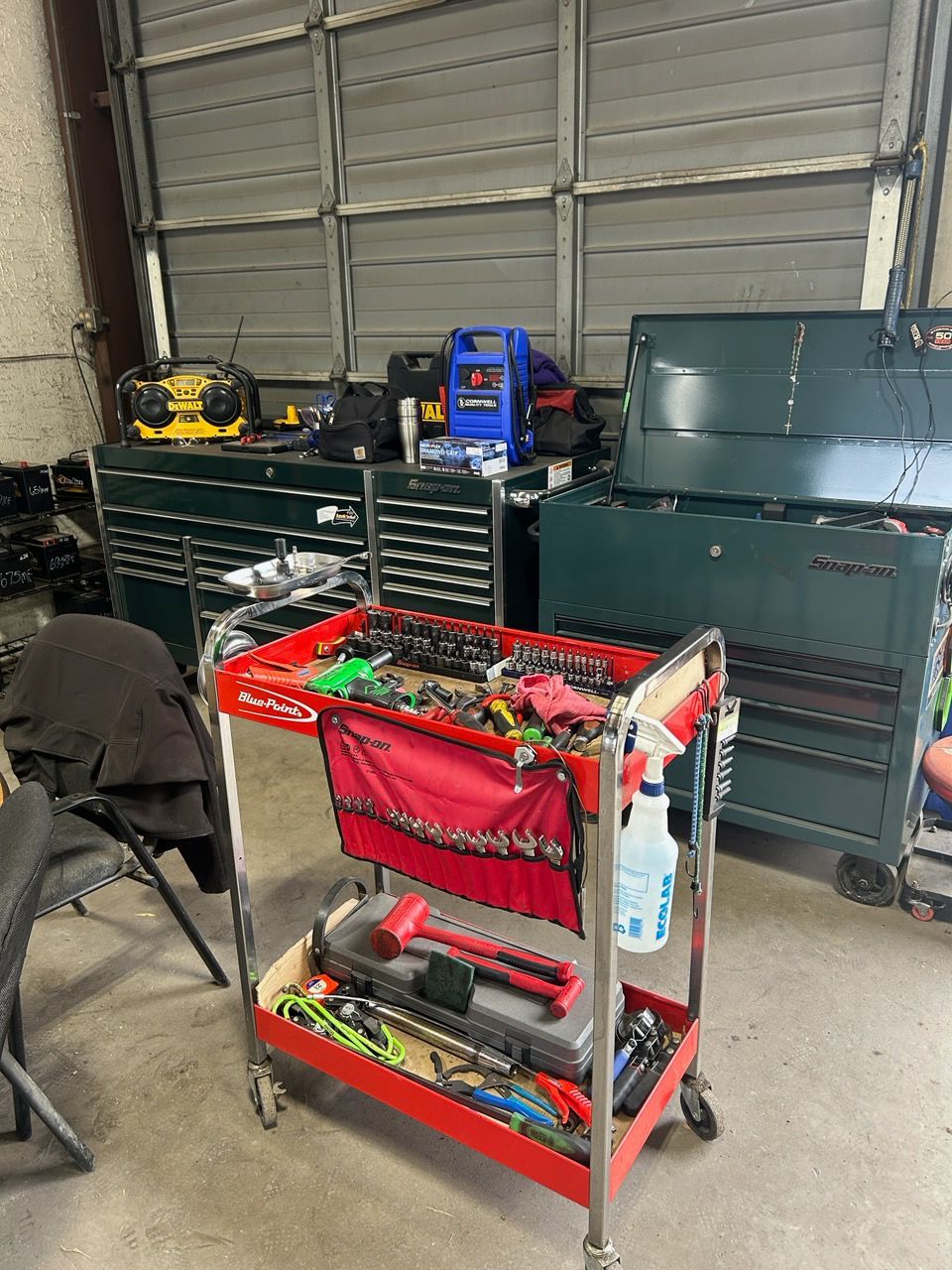 Red rolling tool cart with hand tools in a garage, with tool chests and cases in the background