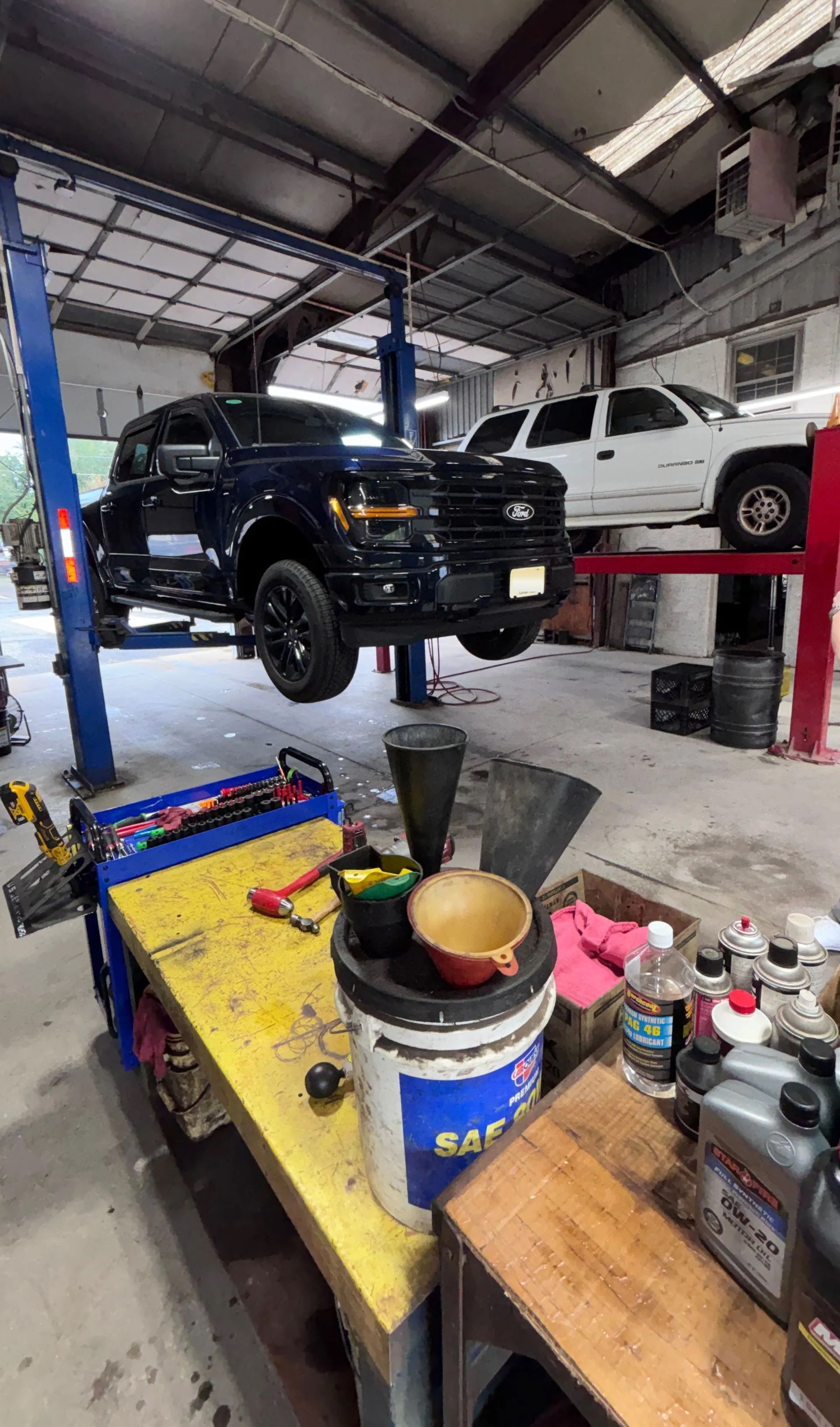 Black pickup truck on a lift in an auto repair shop, with tools and workbench in the foreground