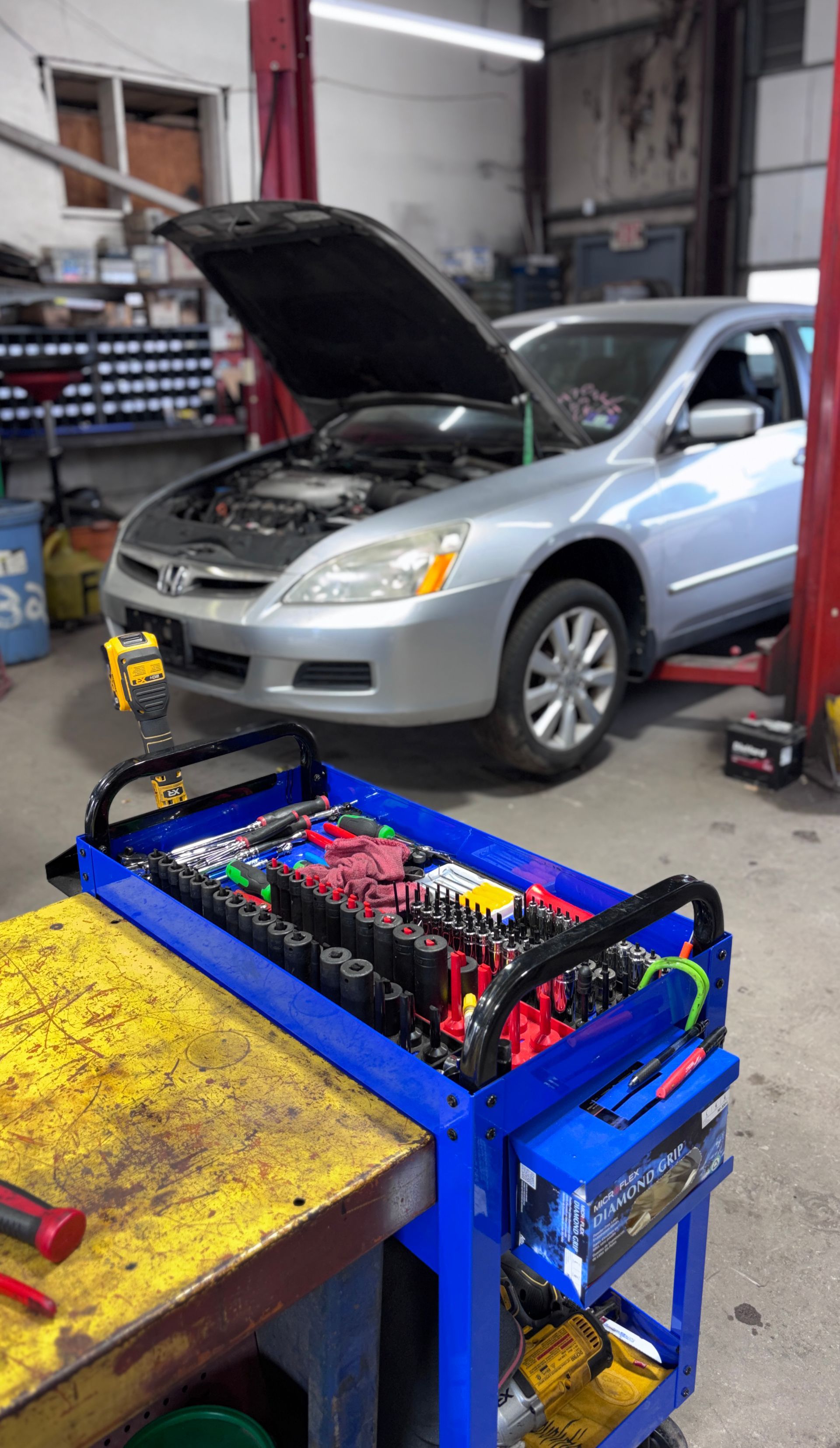 Silver car in a mechanic’s garage with hood open, beside a blue workbench with electronic equipment.