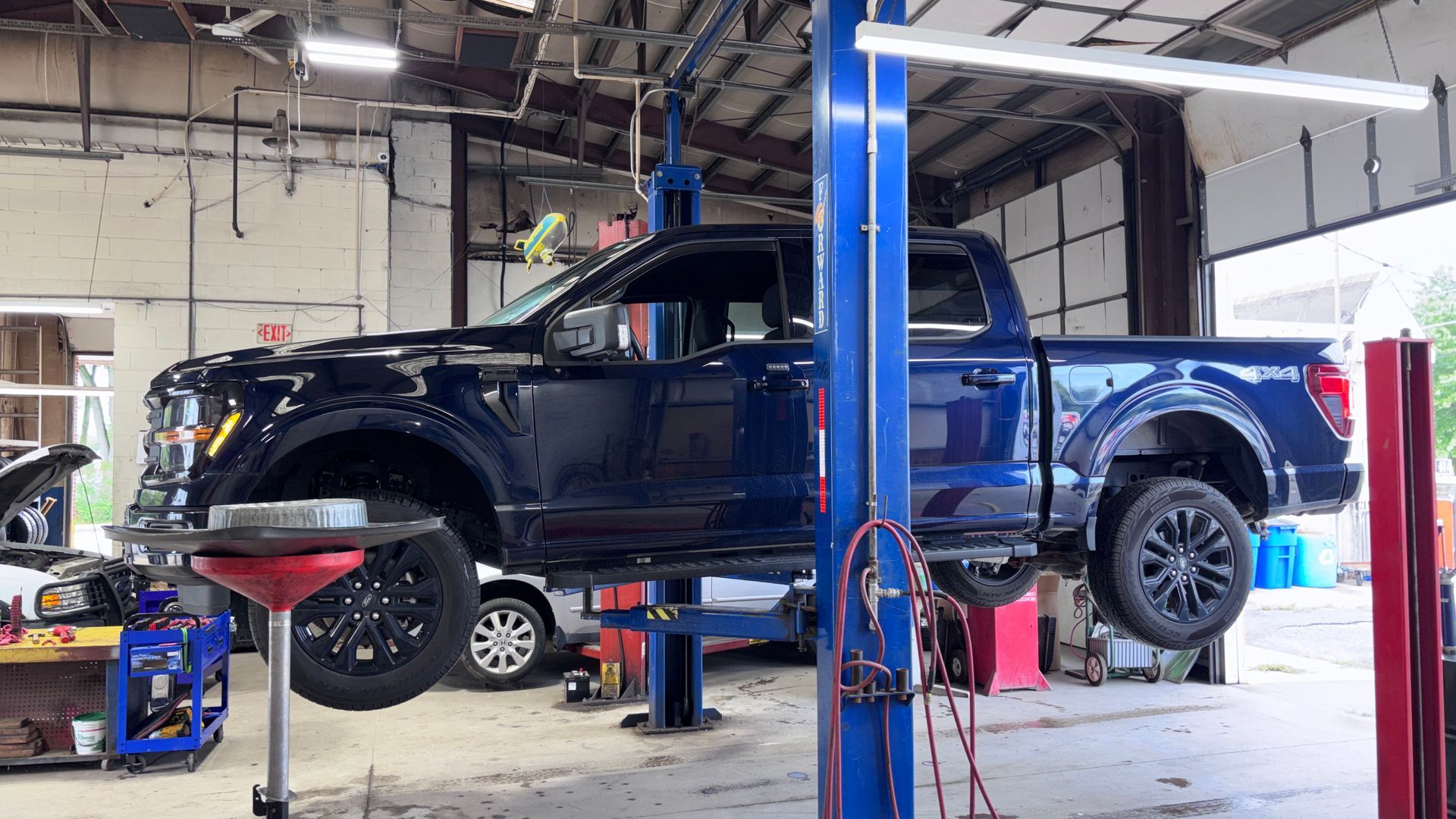 Black pickup truck on a car lift in an auto repair shop, with tools and equipment around it.