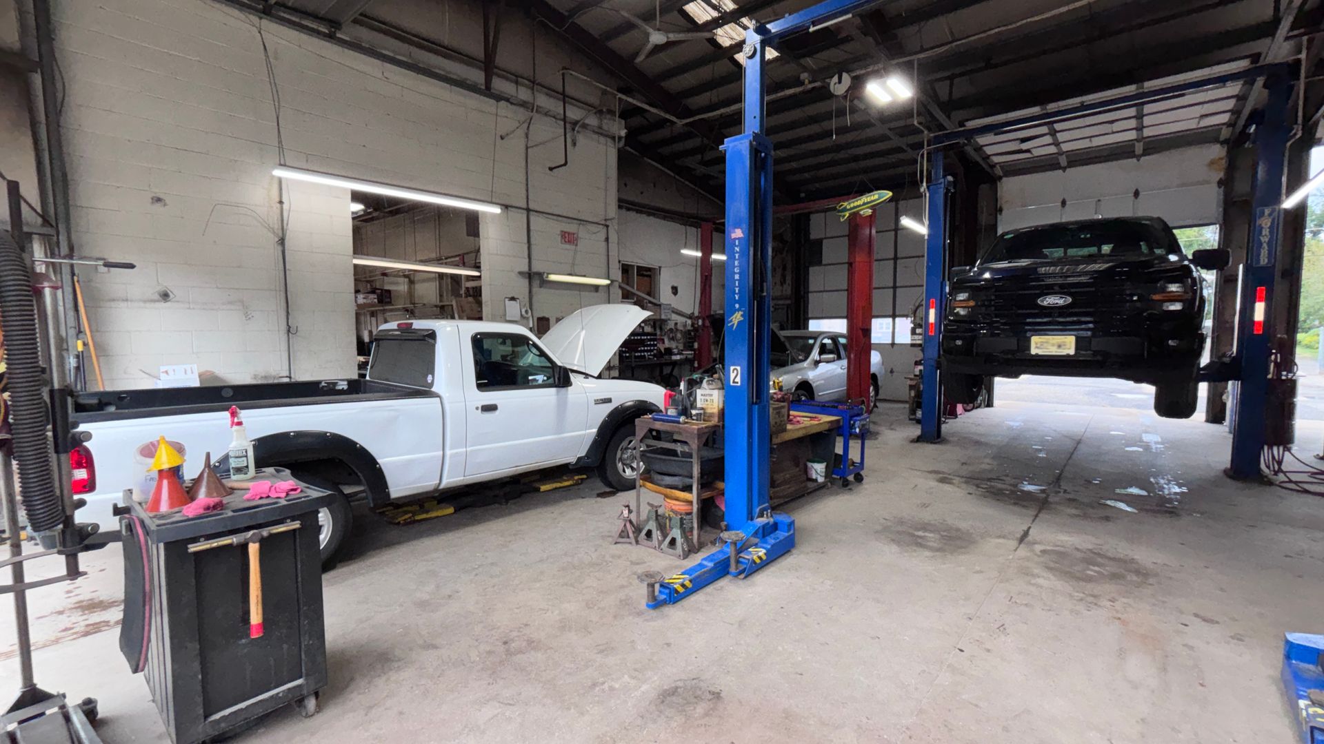 Auto repair shop with a white pickup on a lift and a black SUV in the bay