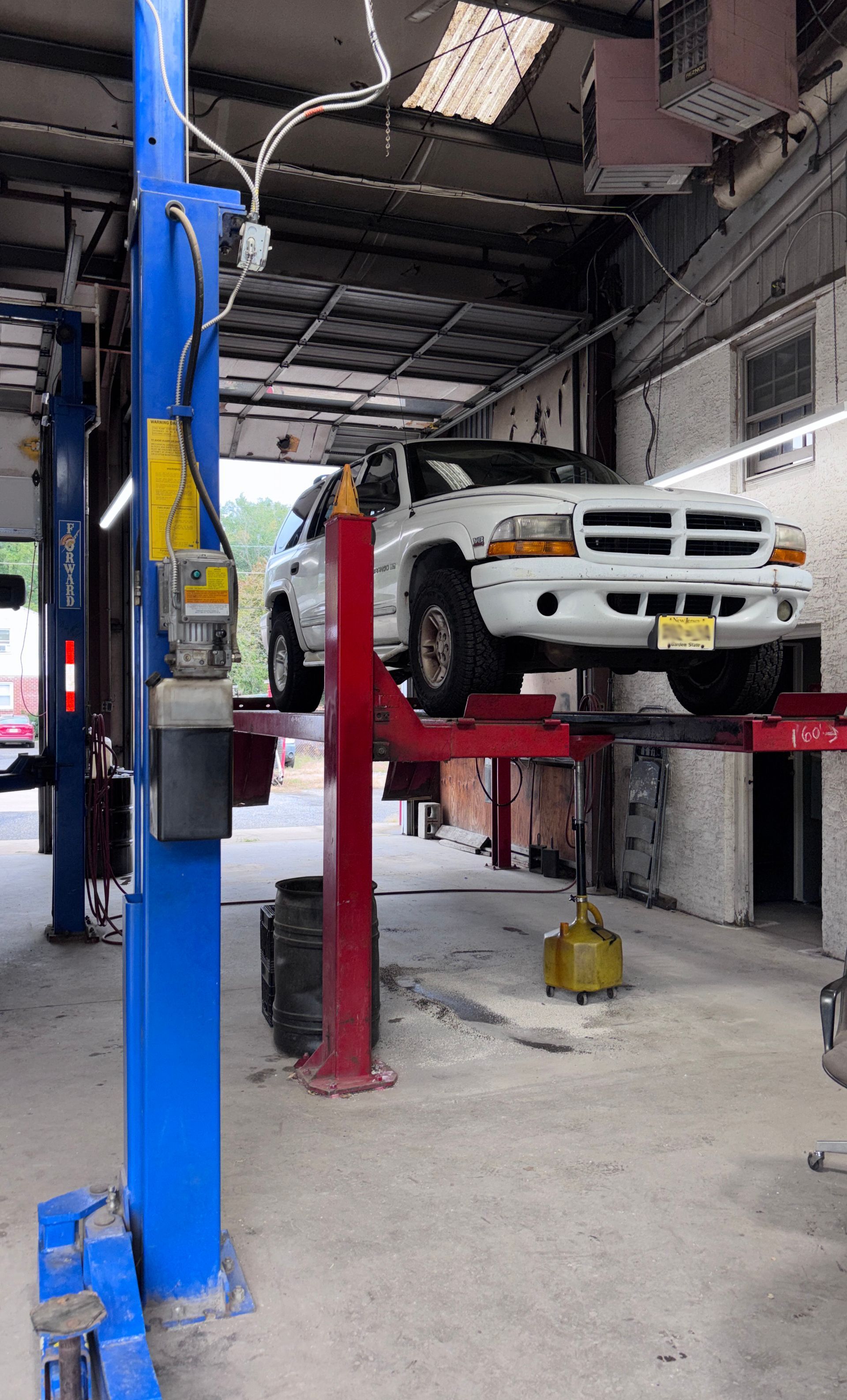 White car on a red lift in an auto repair shop with a blue hydraulic lift nearby