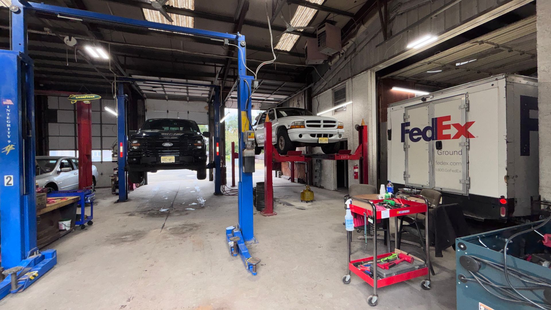 Auto repair shop with a car lifted on blue hoists and a FedEx truck parked inside