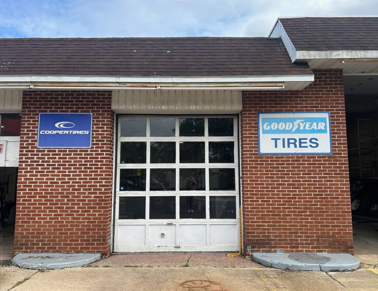 Brick auto shop front with a blue Goodyear Tires sign and white garage door