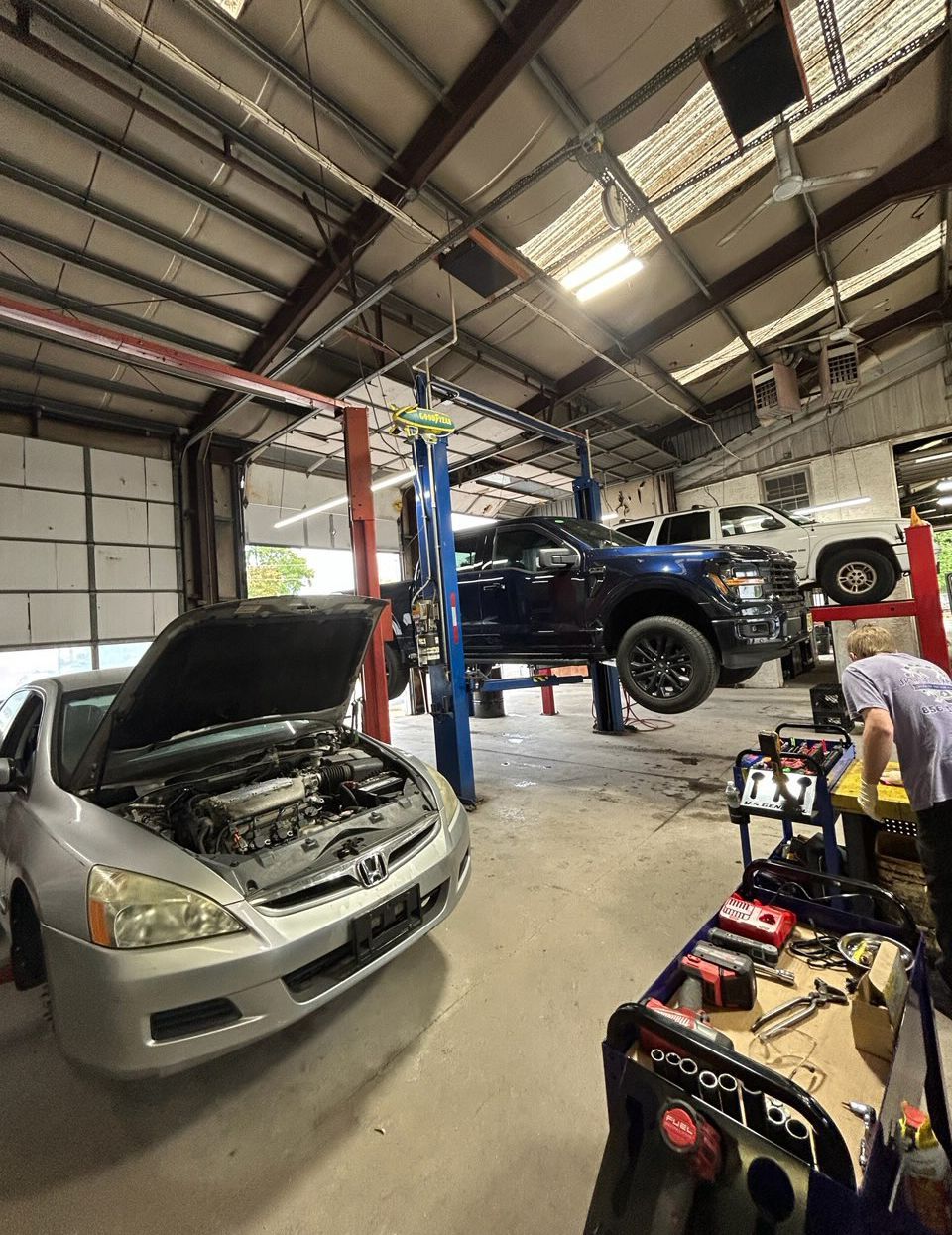 Auto repair shop with several cars lifted on hoists and one silver car with hood open in the foreground