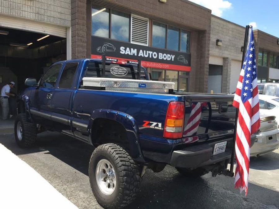 A blue truck is parked in front of sam auto body