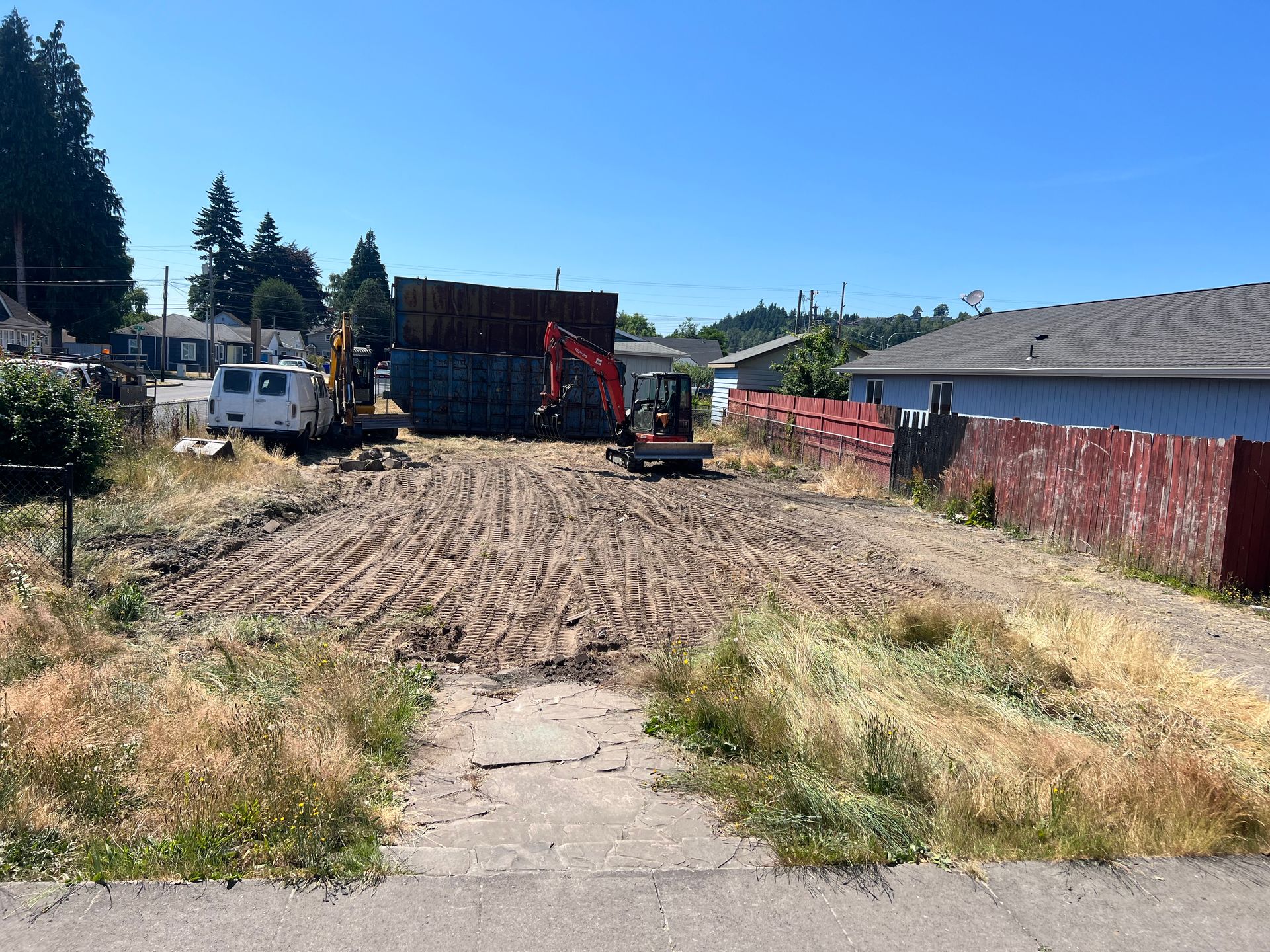 an excavator is working on a dirt road in a residential area