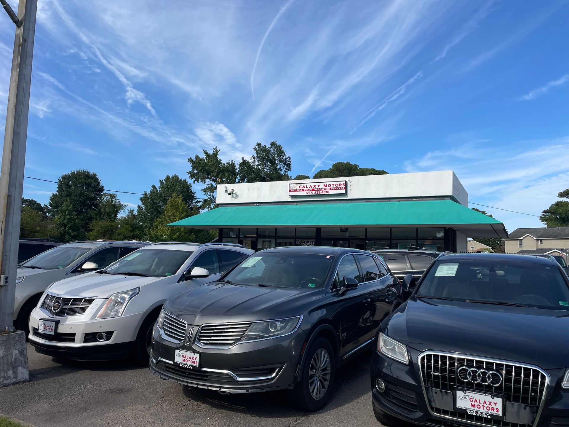 Cars parked in front of a car dealership on a sunny day with a blue sky.