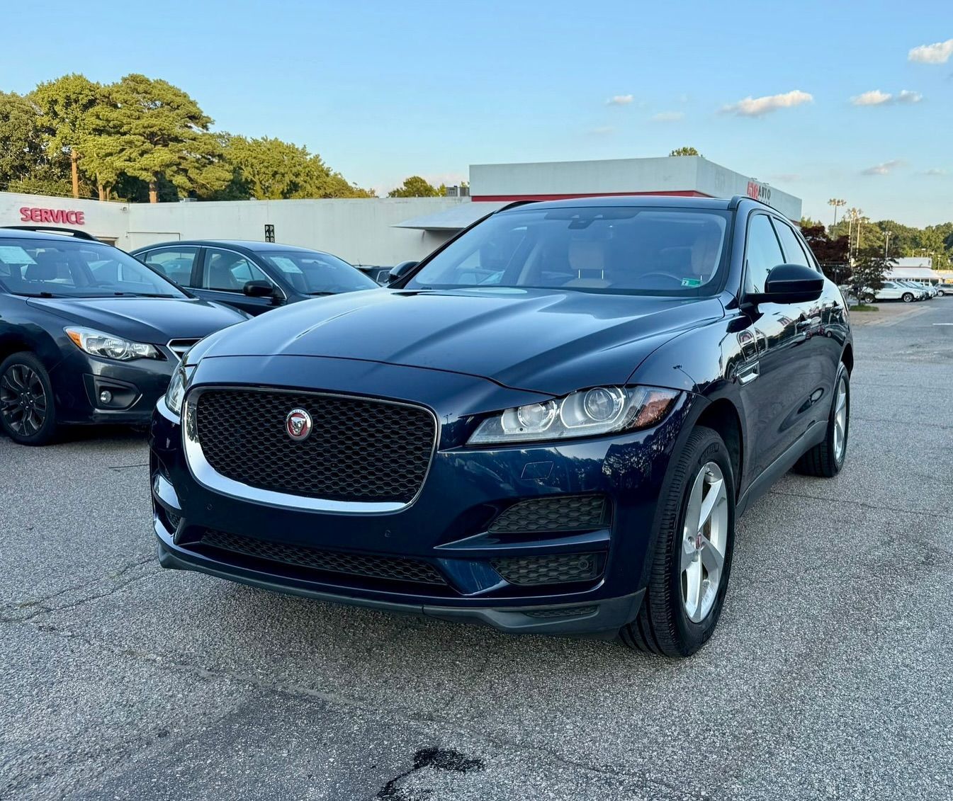 Dark blue Jaguar F-Pace SUV parked outside of a dealership on an asphalt lot.