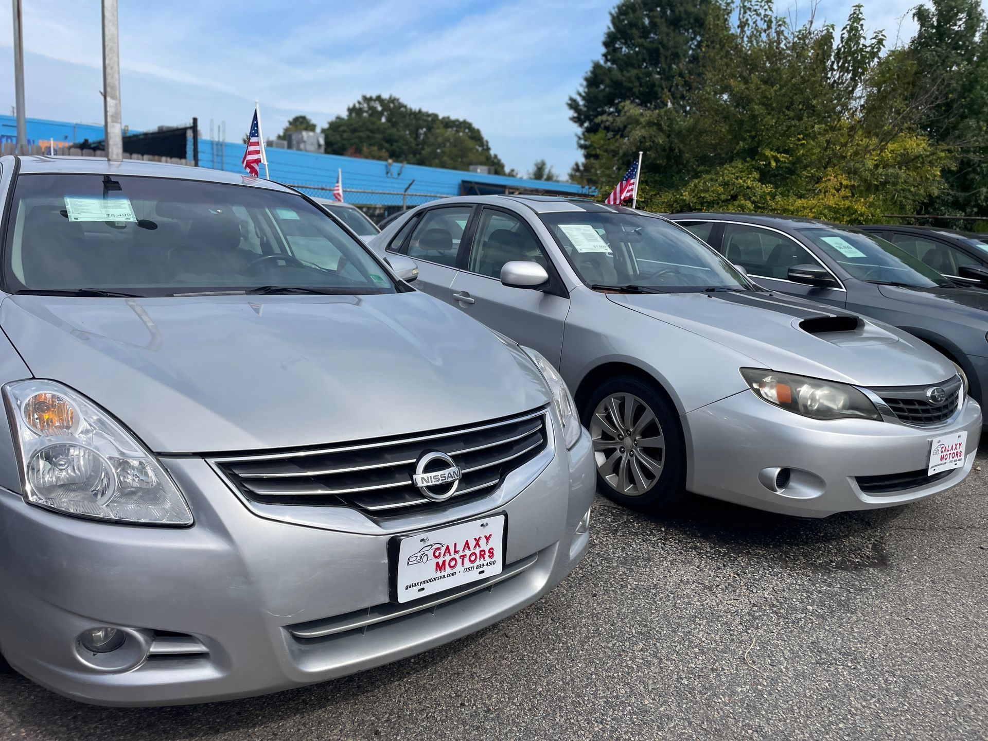 Cars for sale in a car lot: silver Nissan Altima, Subaru Impreza, and other vehicles.