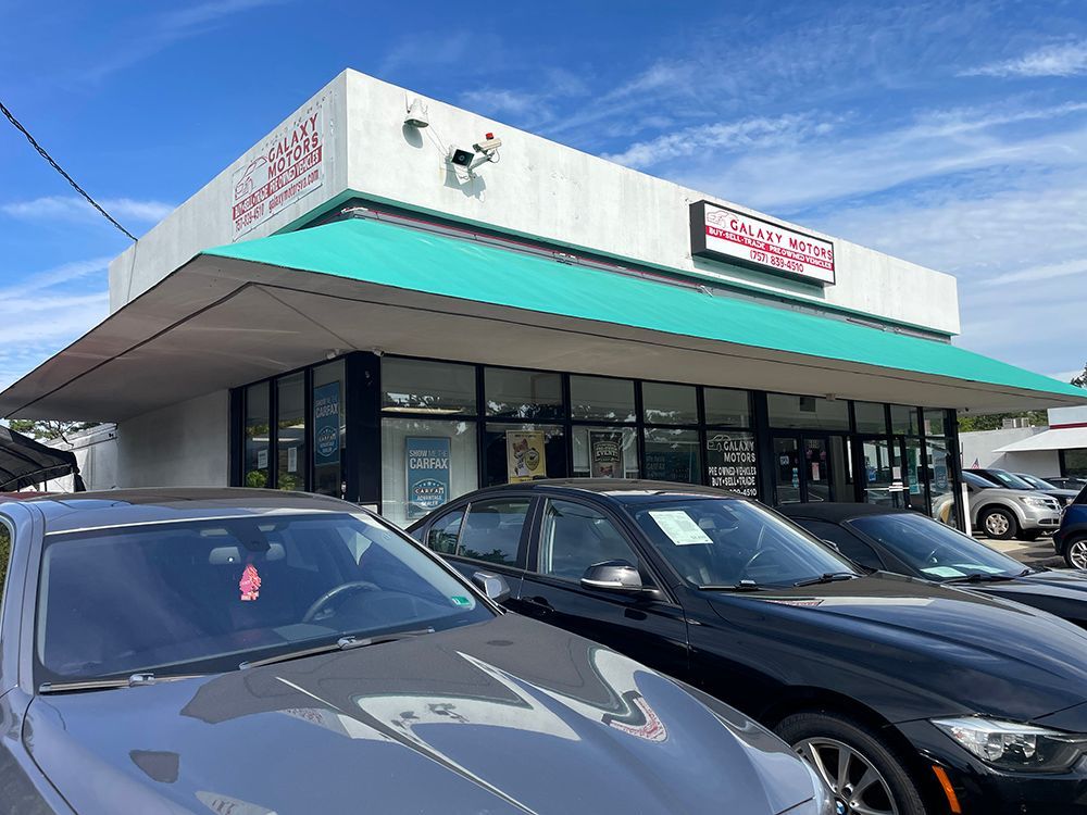 Car dealership exterior with cars parked out front under a teal awning.