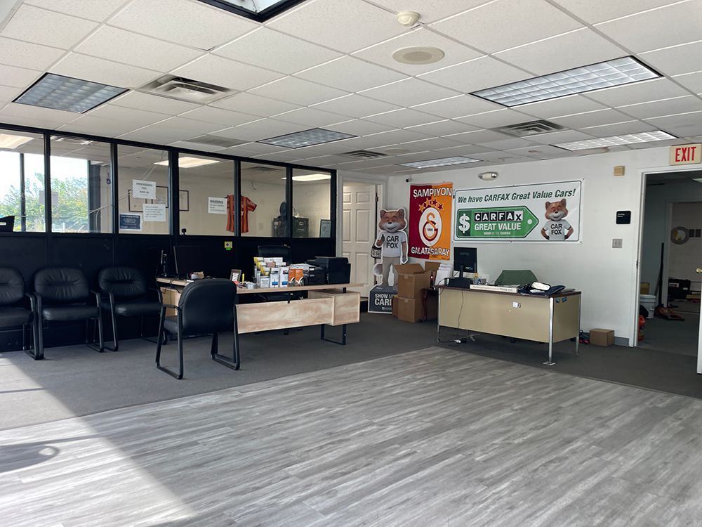 Interior view of an office with desks, chairs, and a waiting area. Sunlight streams in, illuminating the space.